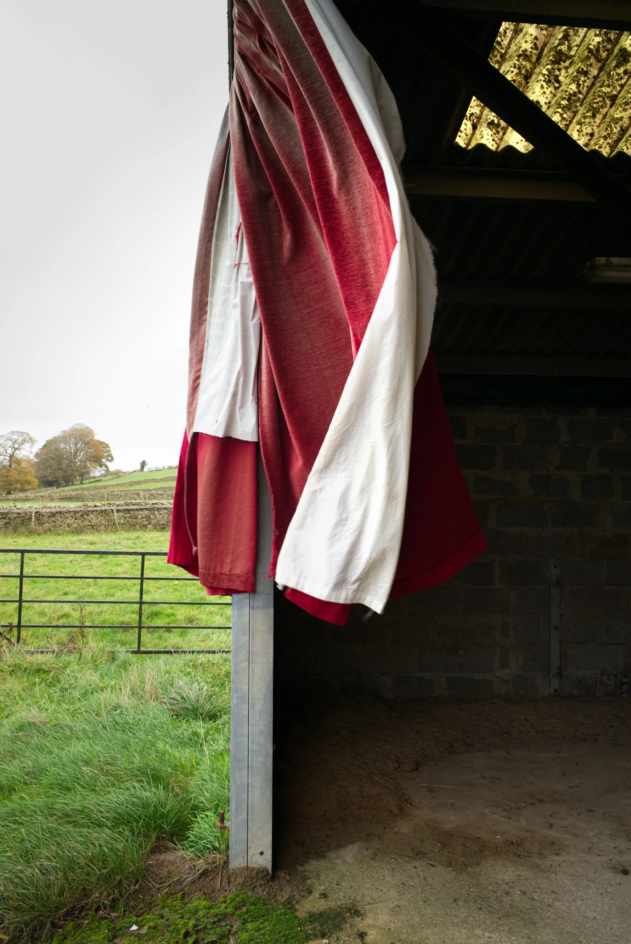 Red and white curtains hanging in the open doorway of a farm outbuilding