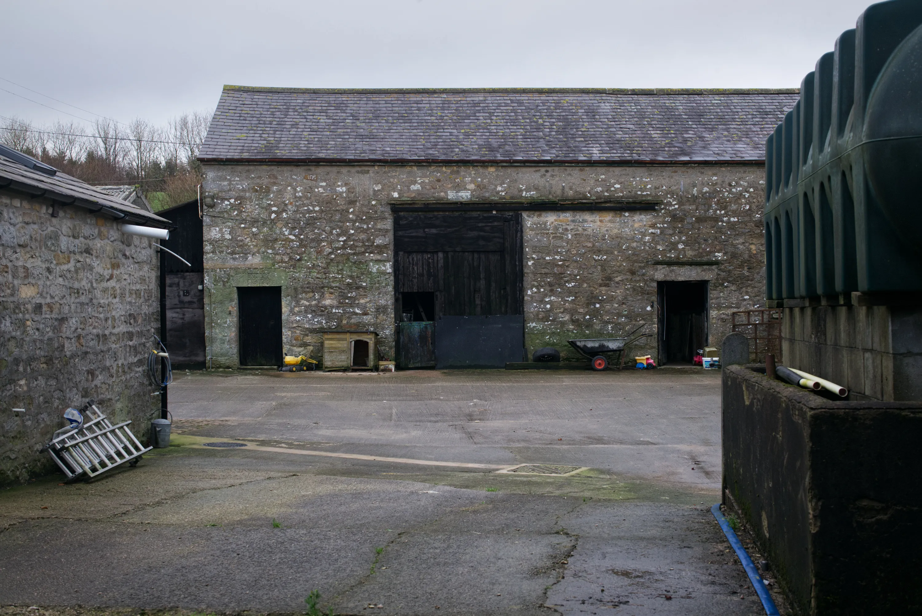 Wide farmyard with a large stone barn, scattered equipment, and overcast sky