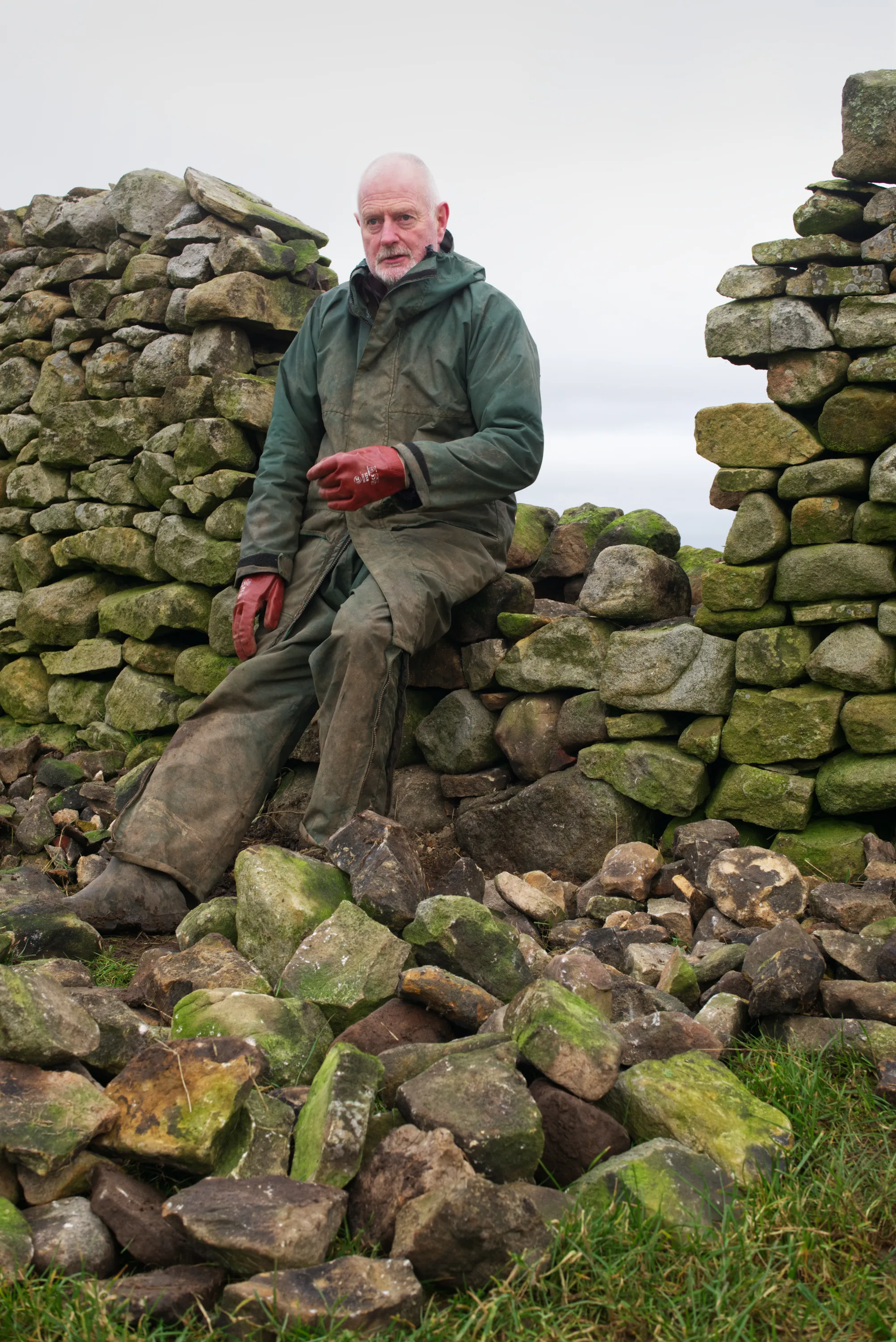 Man in work gear seated on a pile of stones beside a gap in a dry stone wall