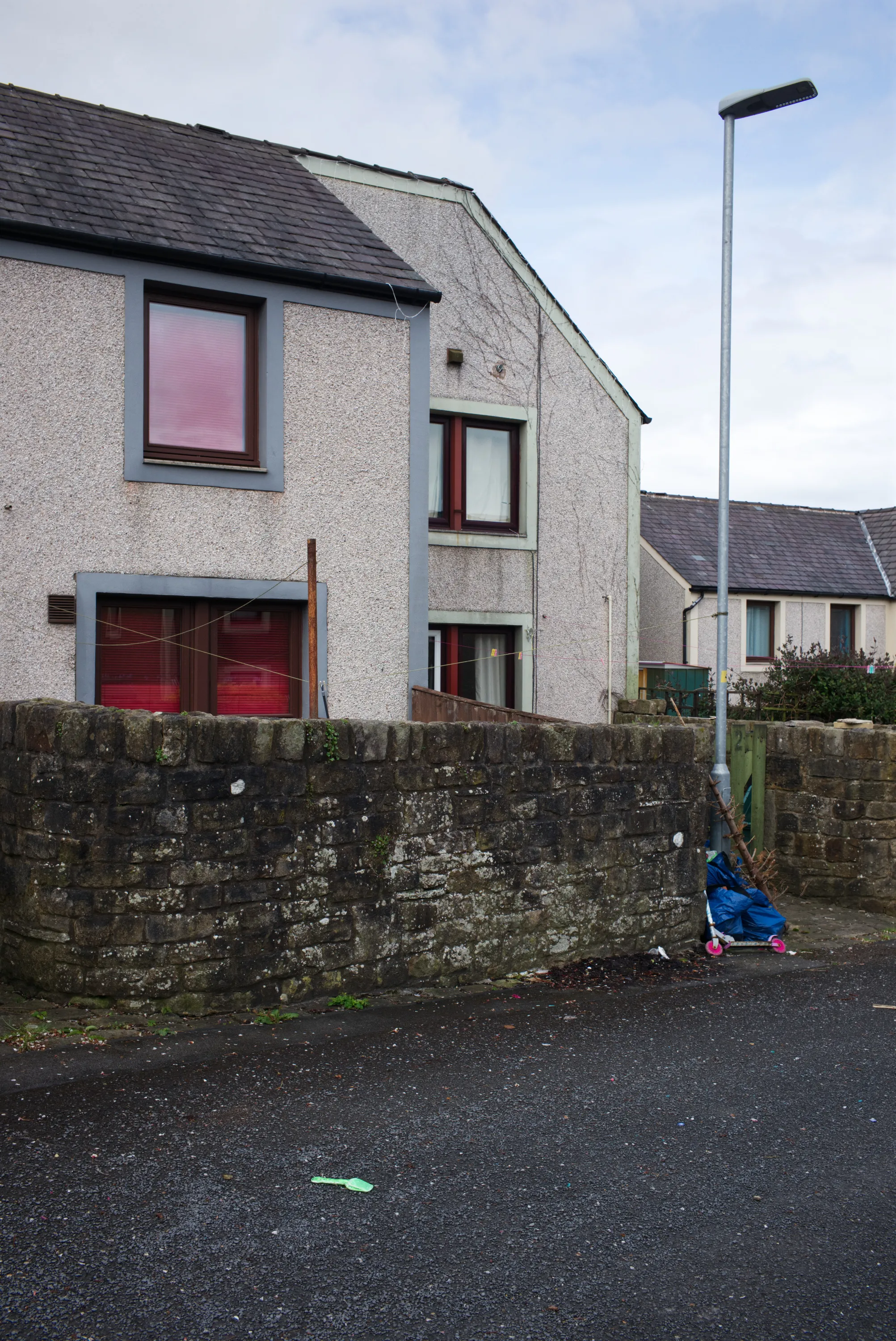 Render-clad semi-detached house behind a mossy stone wall, a child's scooter leaning at the base of a lamppost