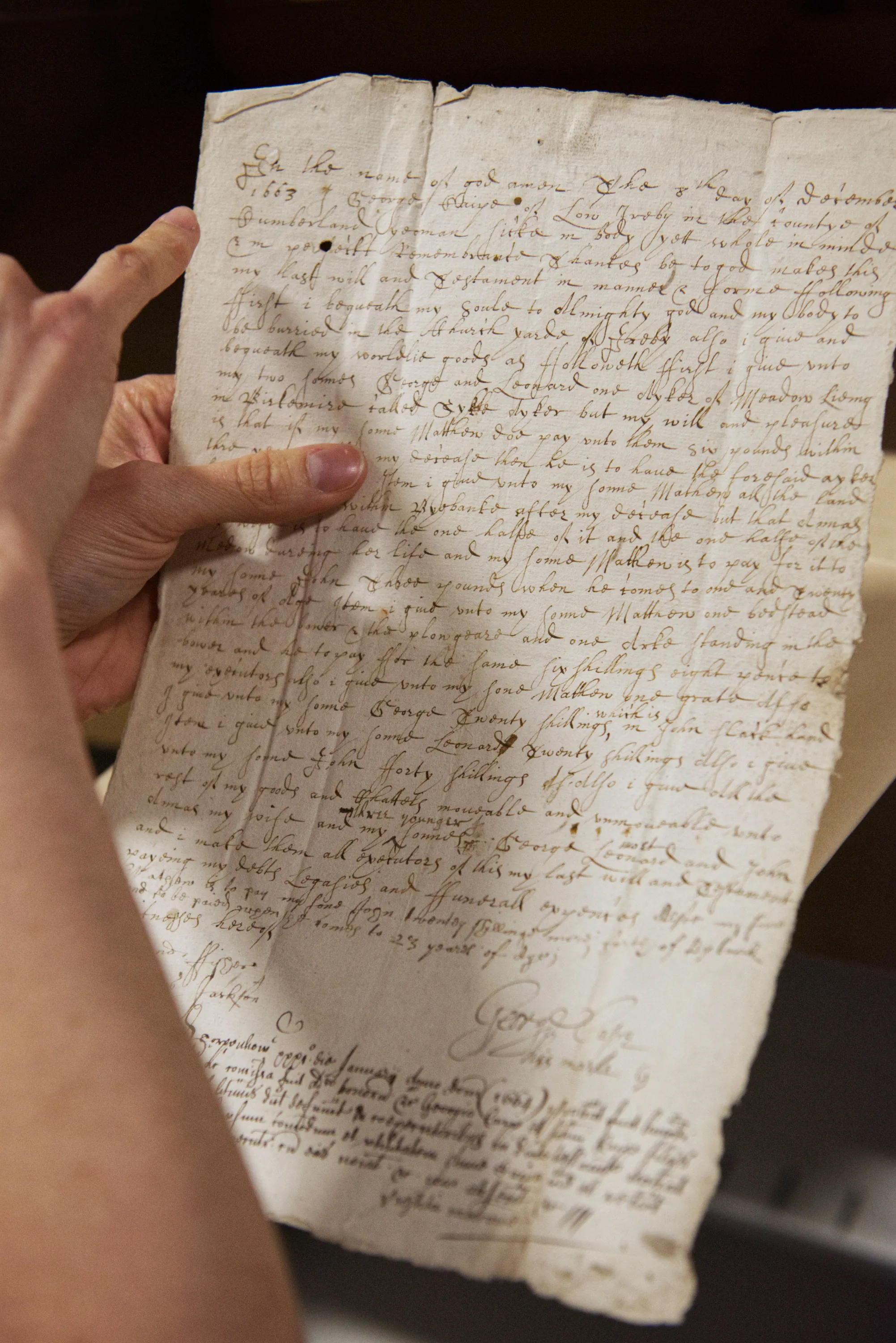 A hand holds an aged handwritten document, its ink faded and paper worn with age