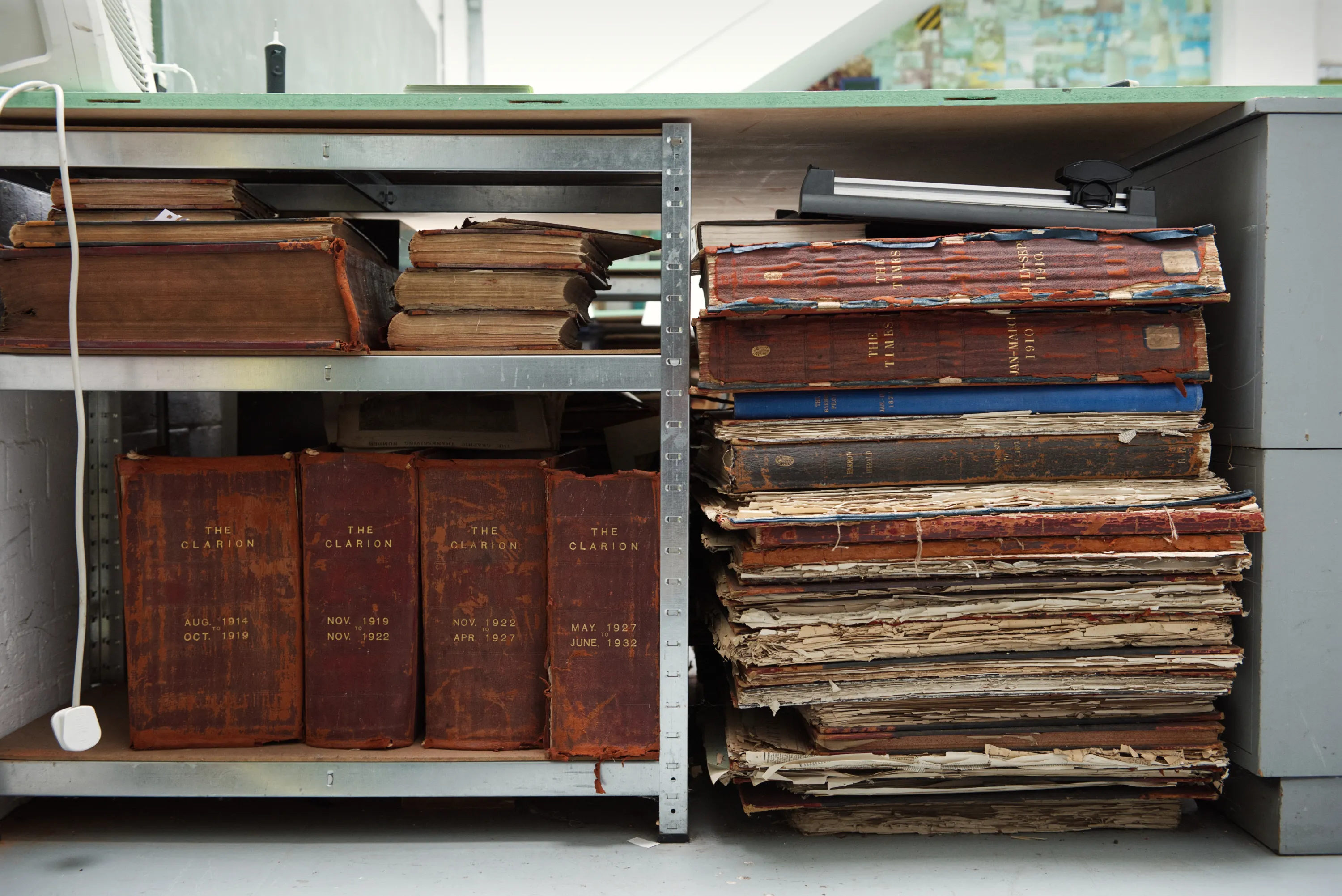 Shelves holding bound volumes of The Clarion newspaper from the 1910s to 1930s, alongside stacks of deteriorating periodicals