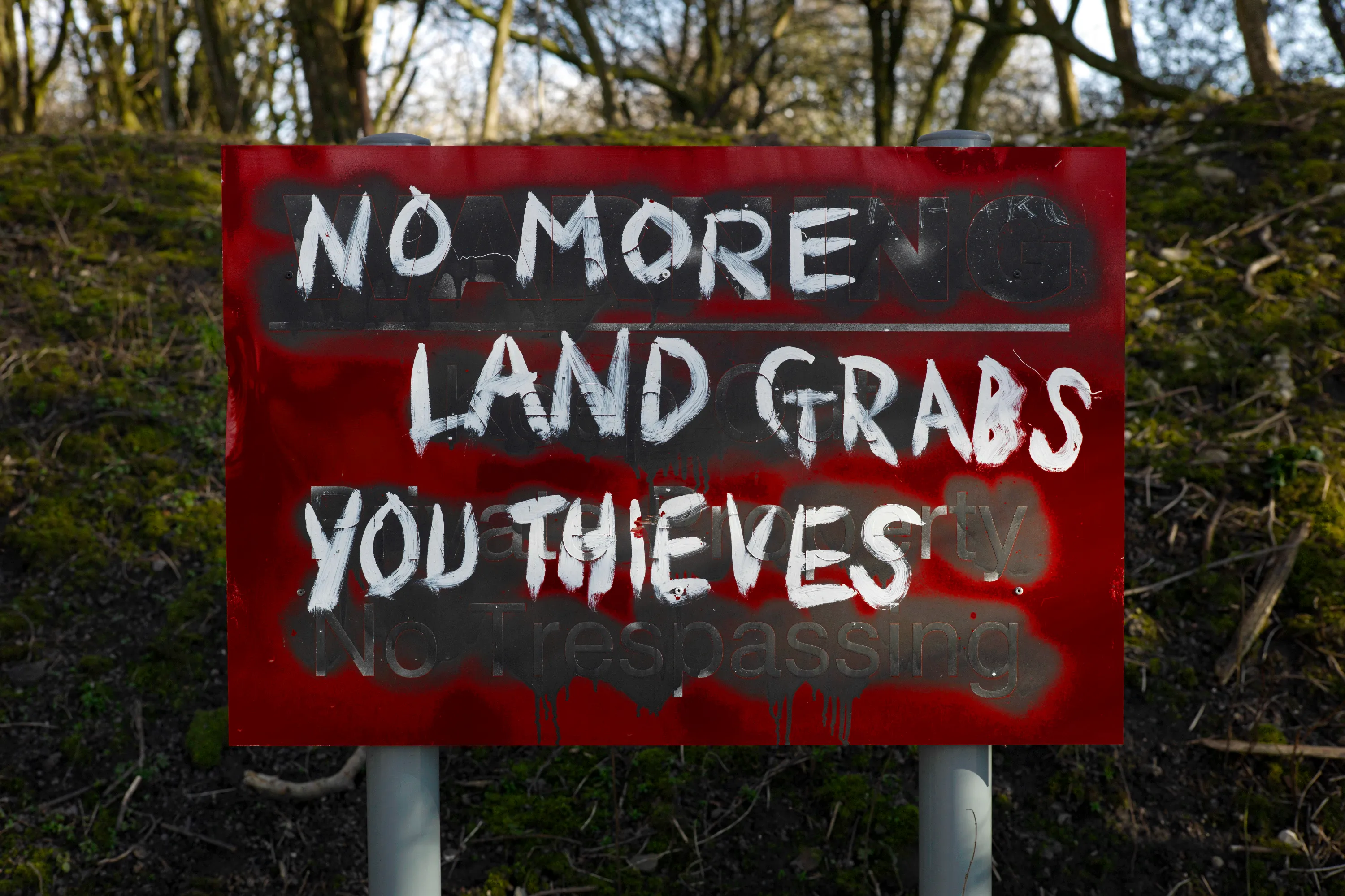 Red sign spray-painted with No more land grabs you thieves over original text