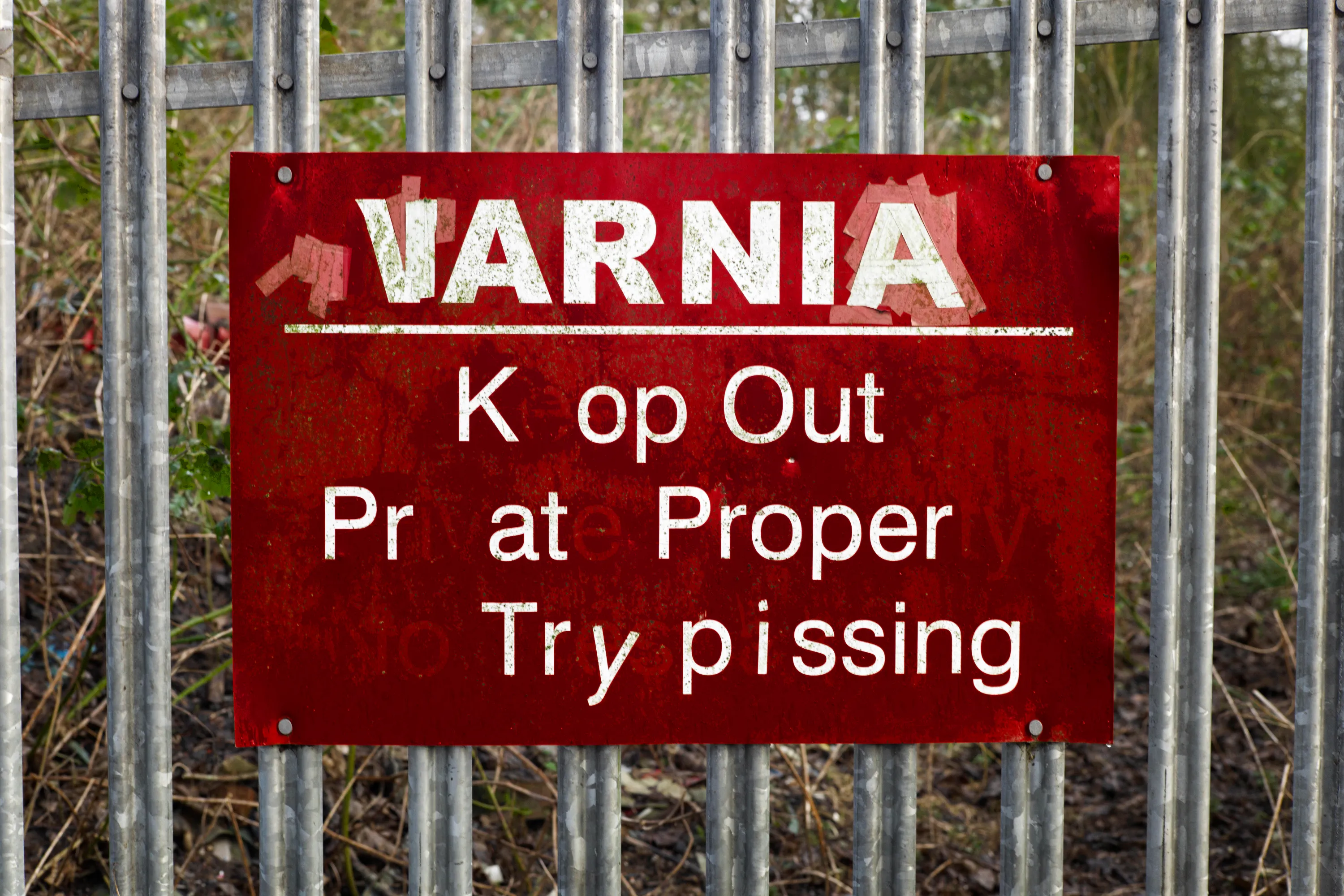 Red warning sign on metal railings with letters obscured by vandalism