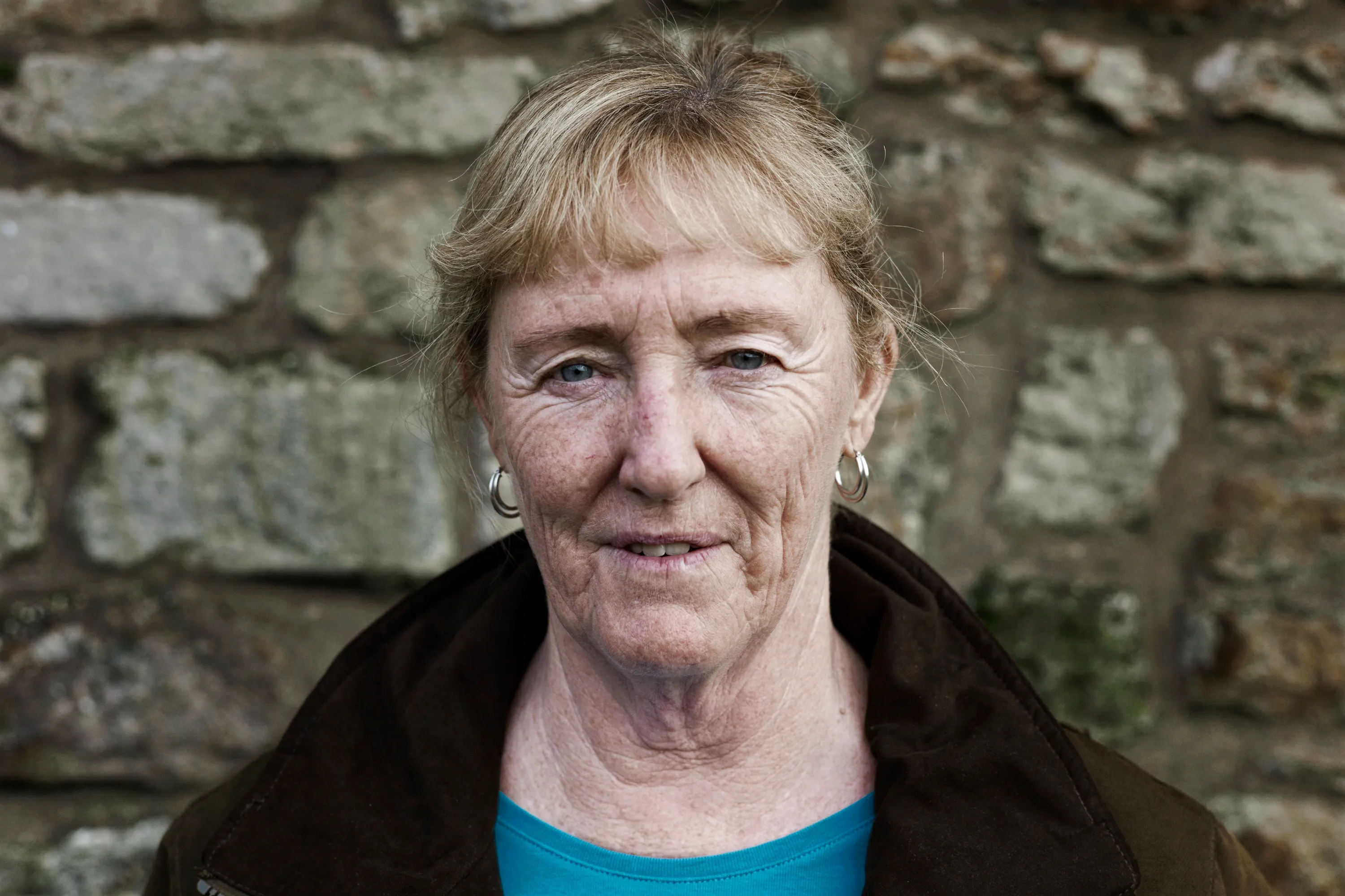 Close portrait of a woman with hoop earrings against a stone wall