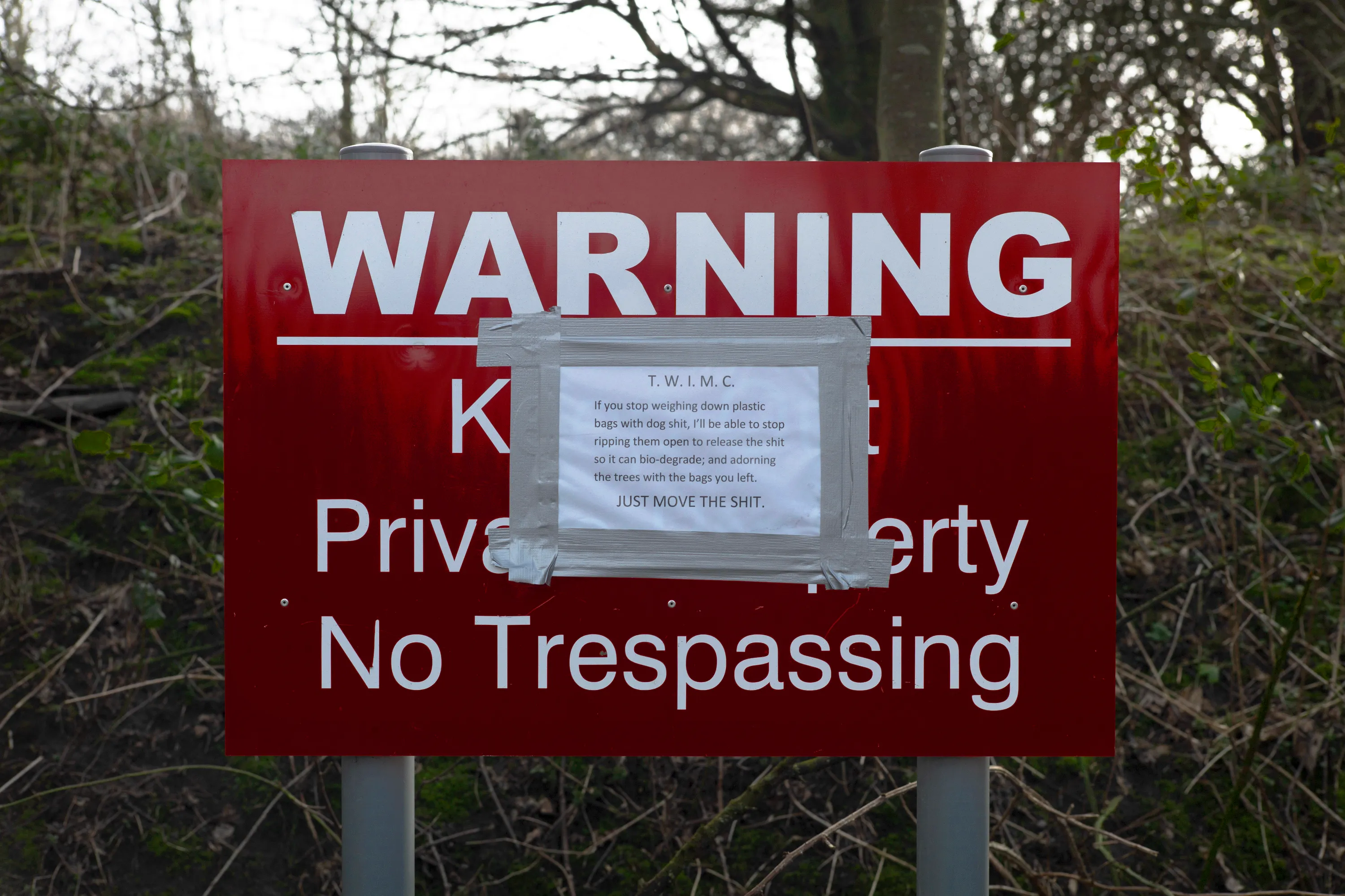 Red Warning — Private Property, No Trespassing sign with a handwritten note taped over it