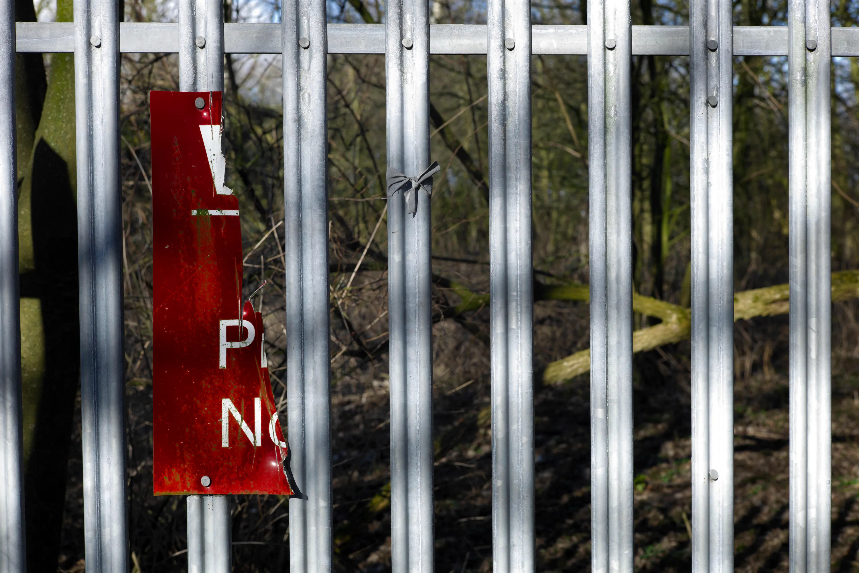 Torn red no-trespassing sign on metal railings, scrubland behind