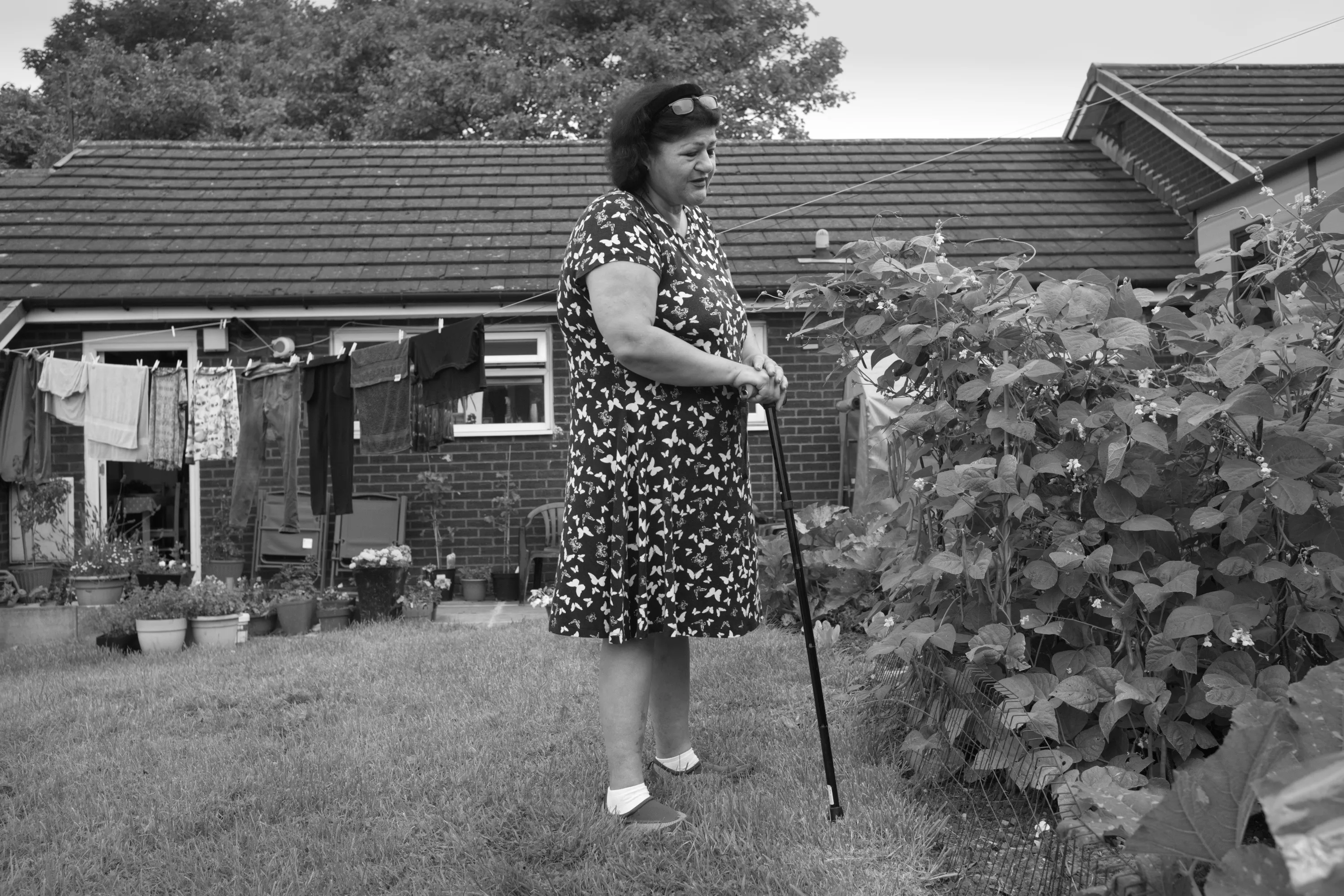 Woman standing in a garden with a walking stick, laundry drying behind her