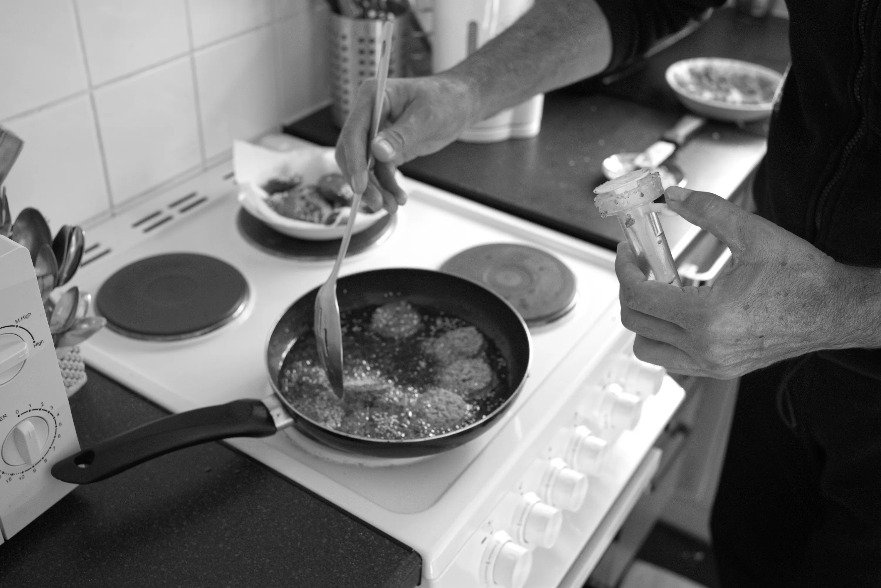 Hands frying falafel in a pan on an electric hob