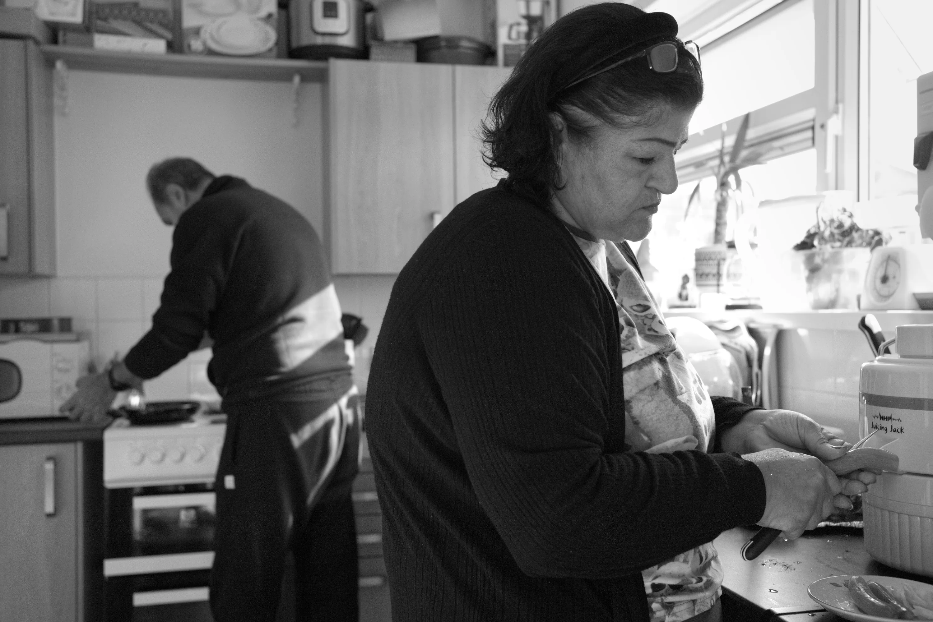 Two people preparing food in a small kitchen, one at the hob and one at the counter