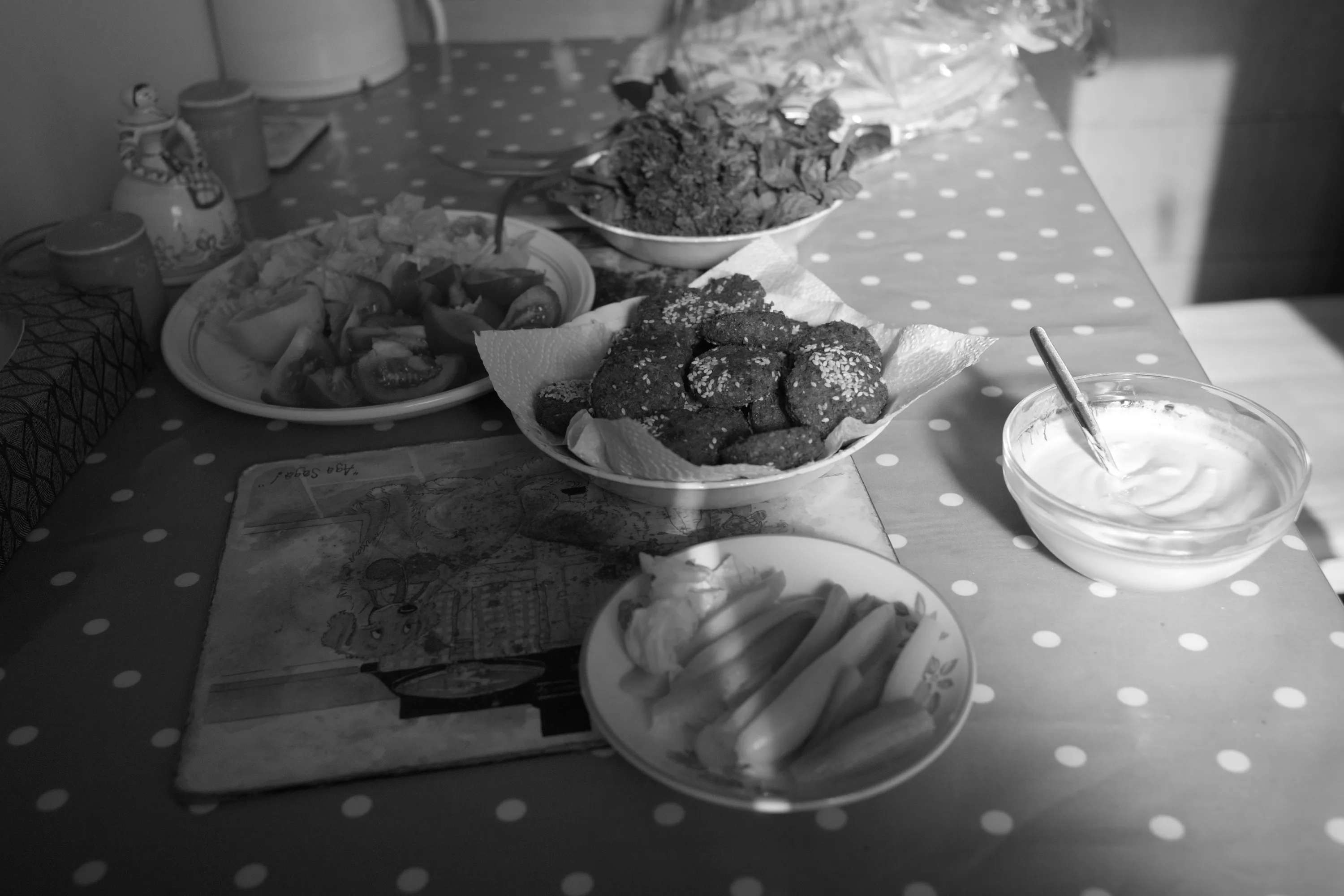 Bowls of falafel, salad, sliced vegetables, and tahini on a polka-dot tablecloth