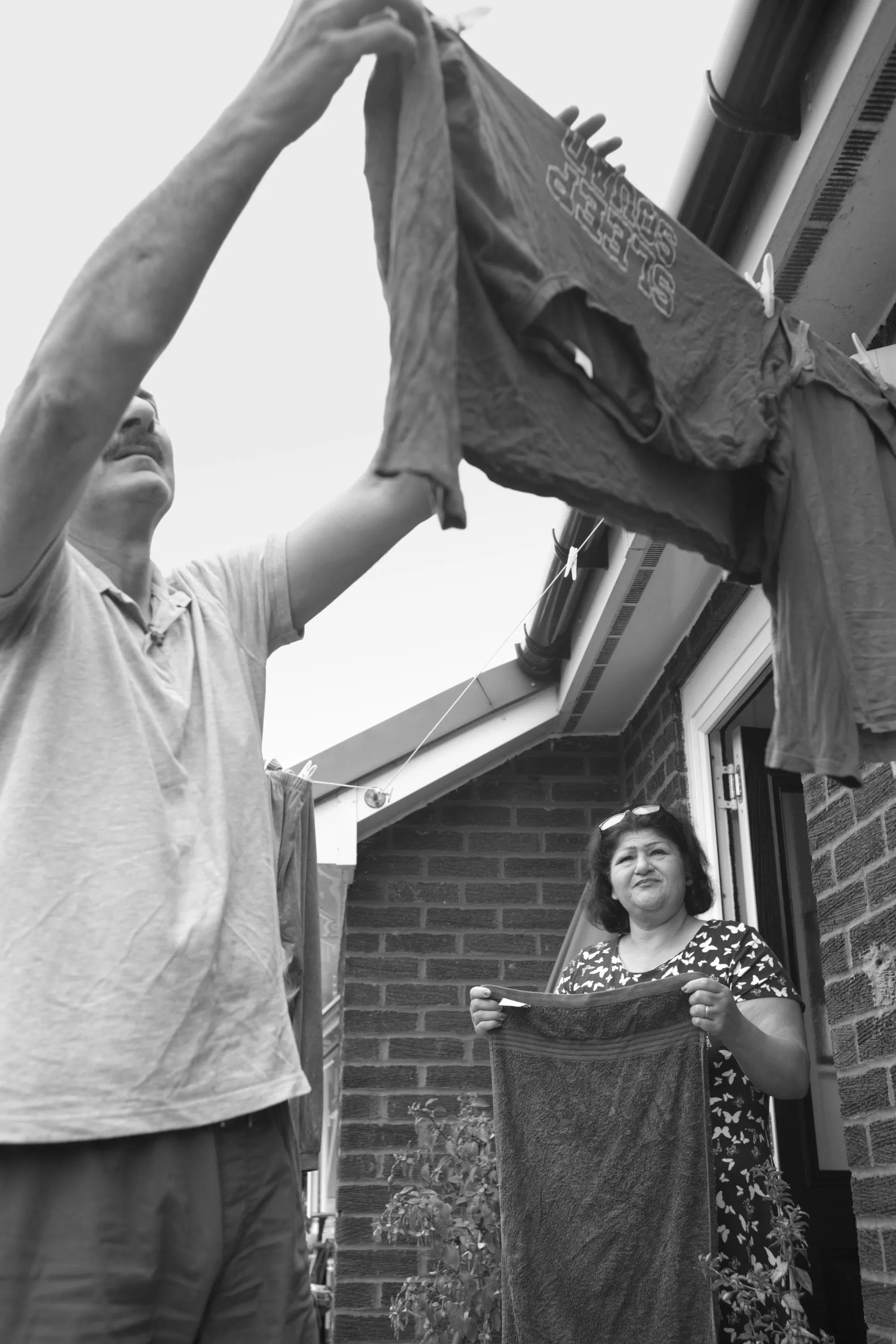 Man and woman hanging laundry on a line outside a brick house