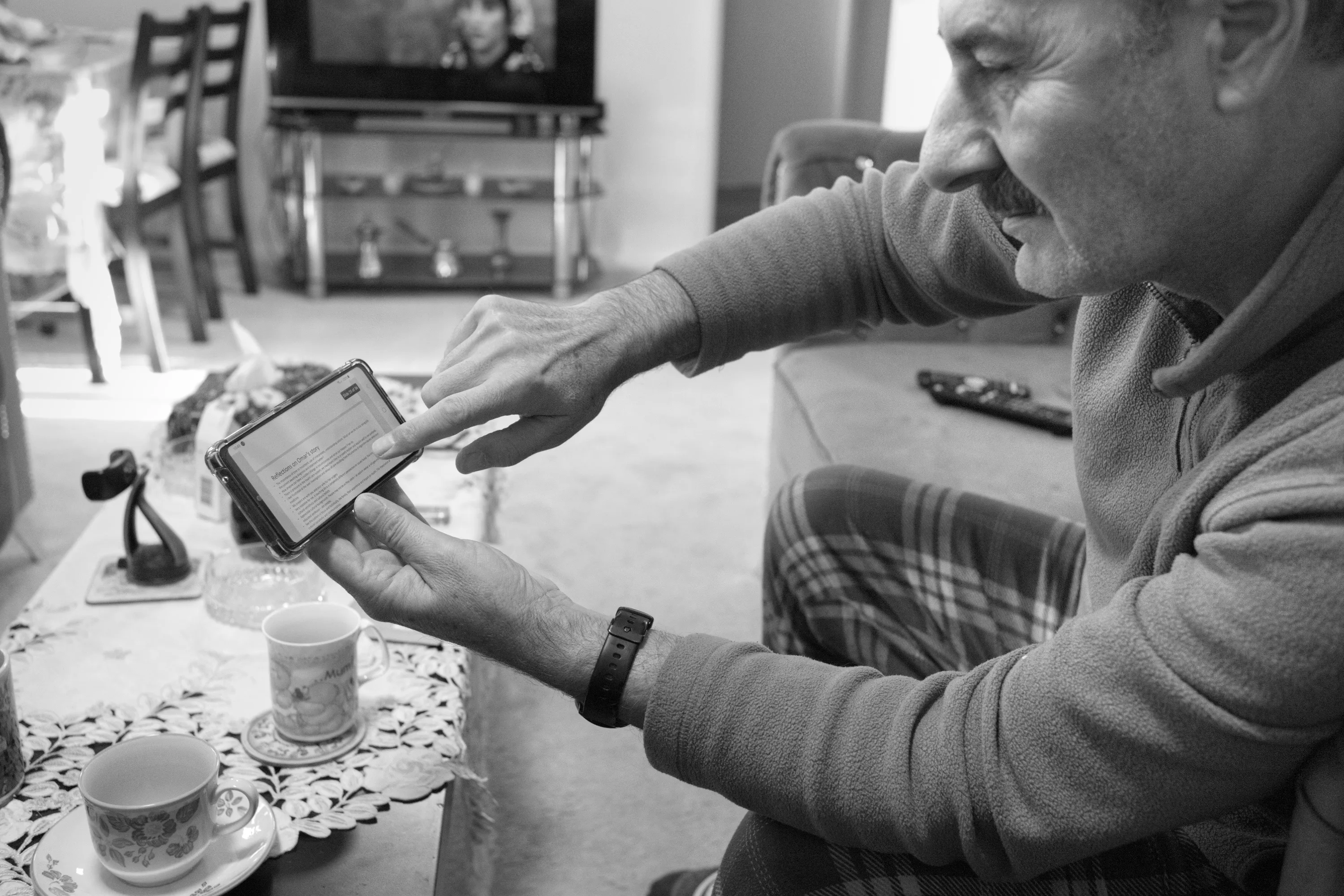 Man sitting indoors pointing at text on a smartphone screen, smiling