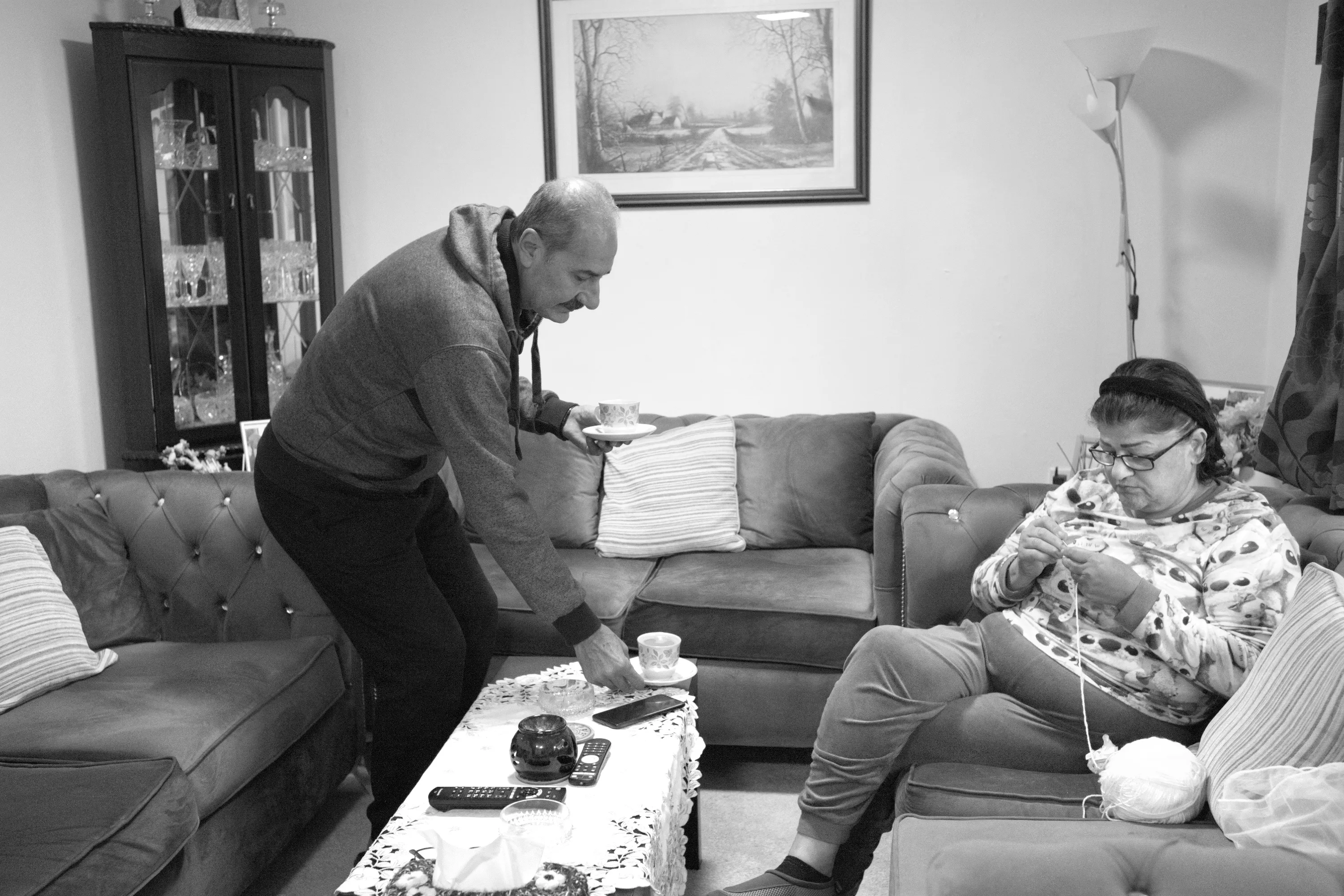Man setting a cup on a coffee table while a woman crochets on the sofa beside him