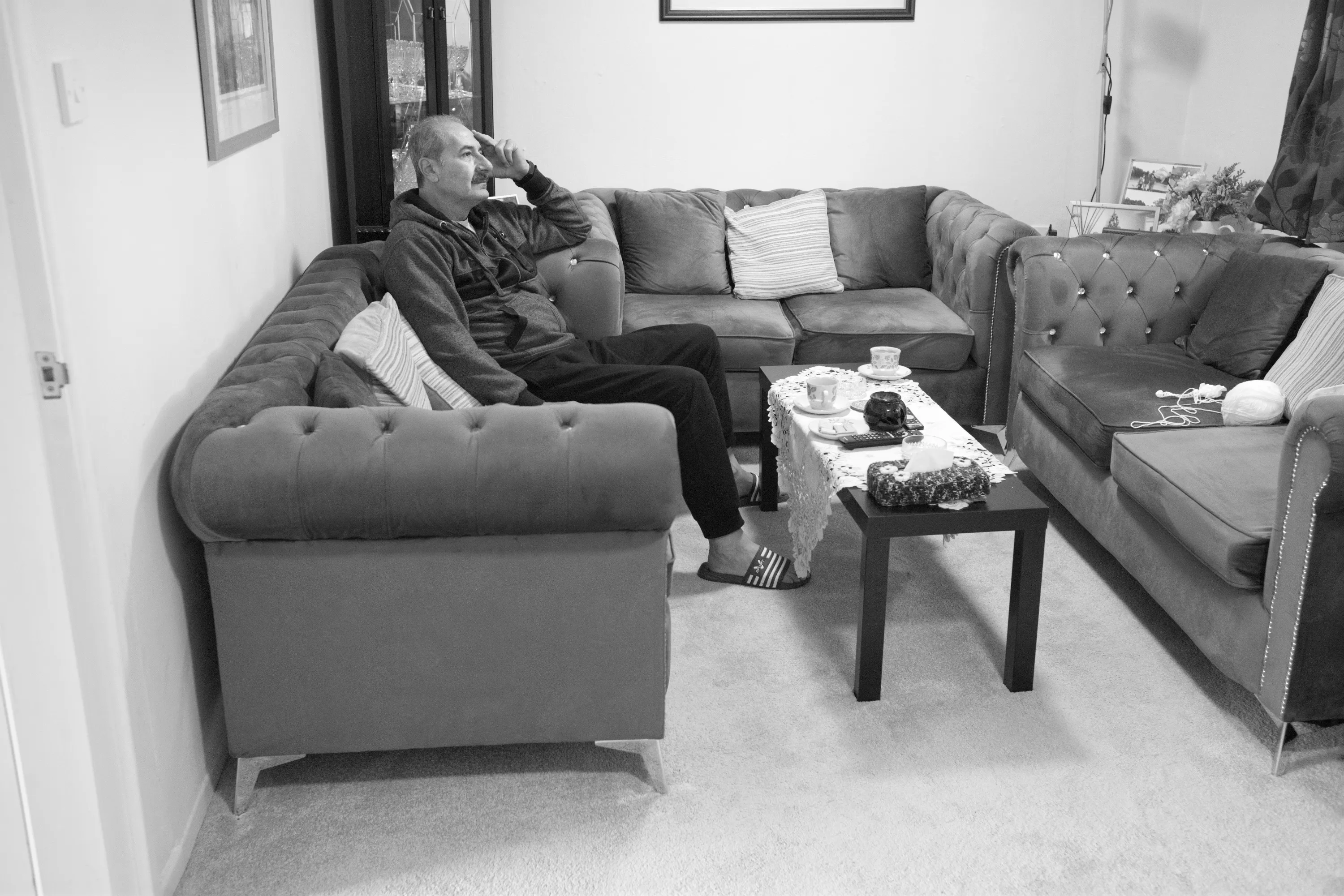 Man seated alone on a corner sofa, resting his hand against his face