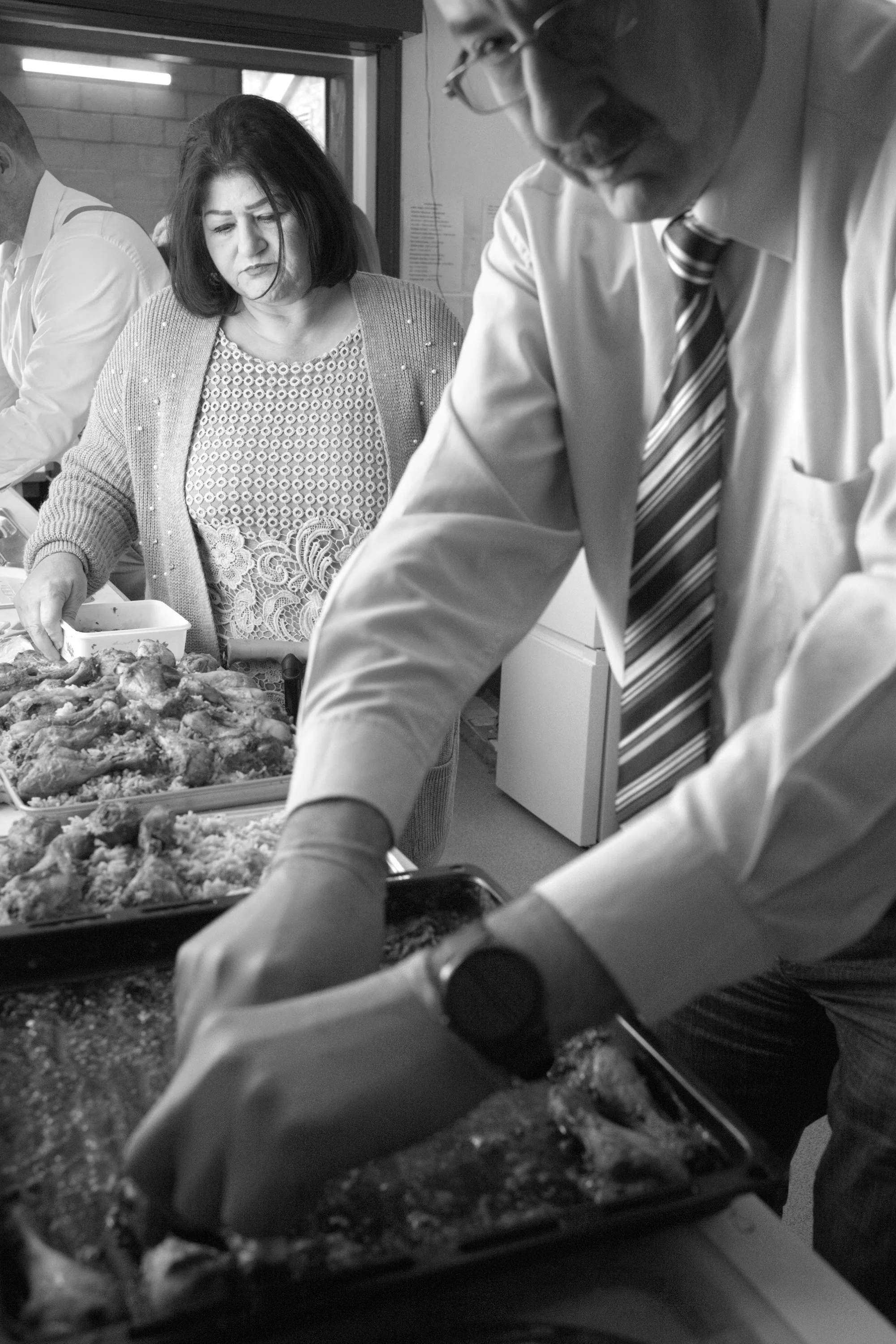 Two people serving food from trays at a communal table