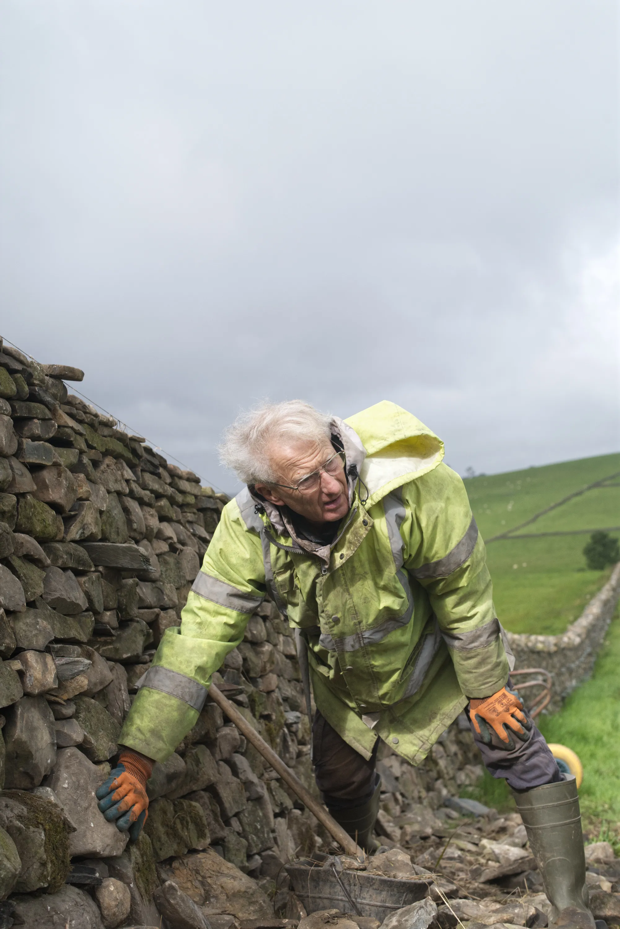 Older man in yellow hi-vis jacket repairs a dry stone wall