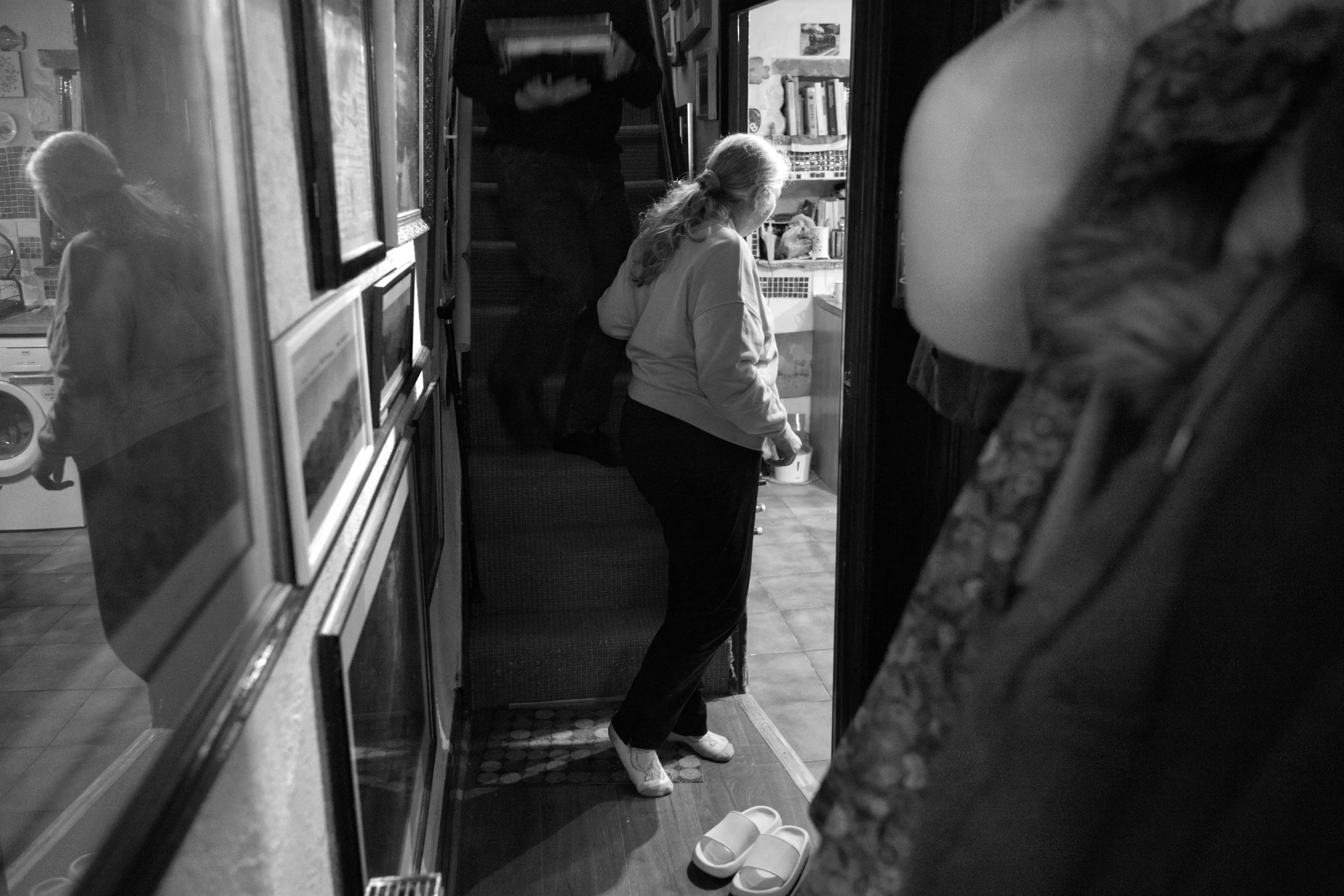 A woman frozen mid-step at the threshold between two rooms, head bowed, unable to move