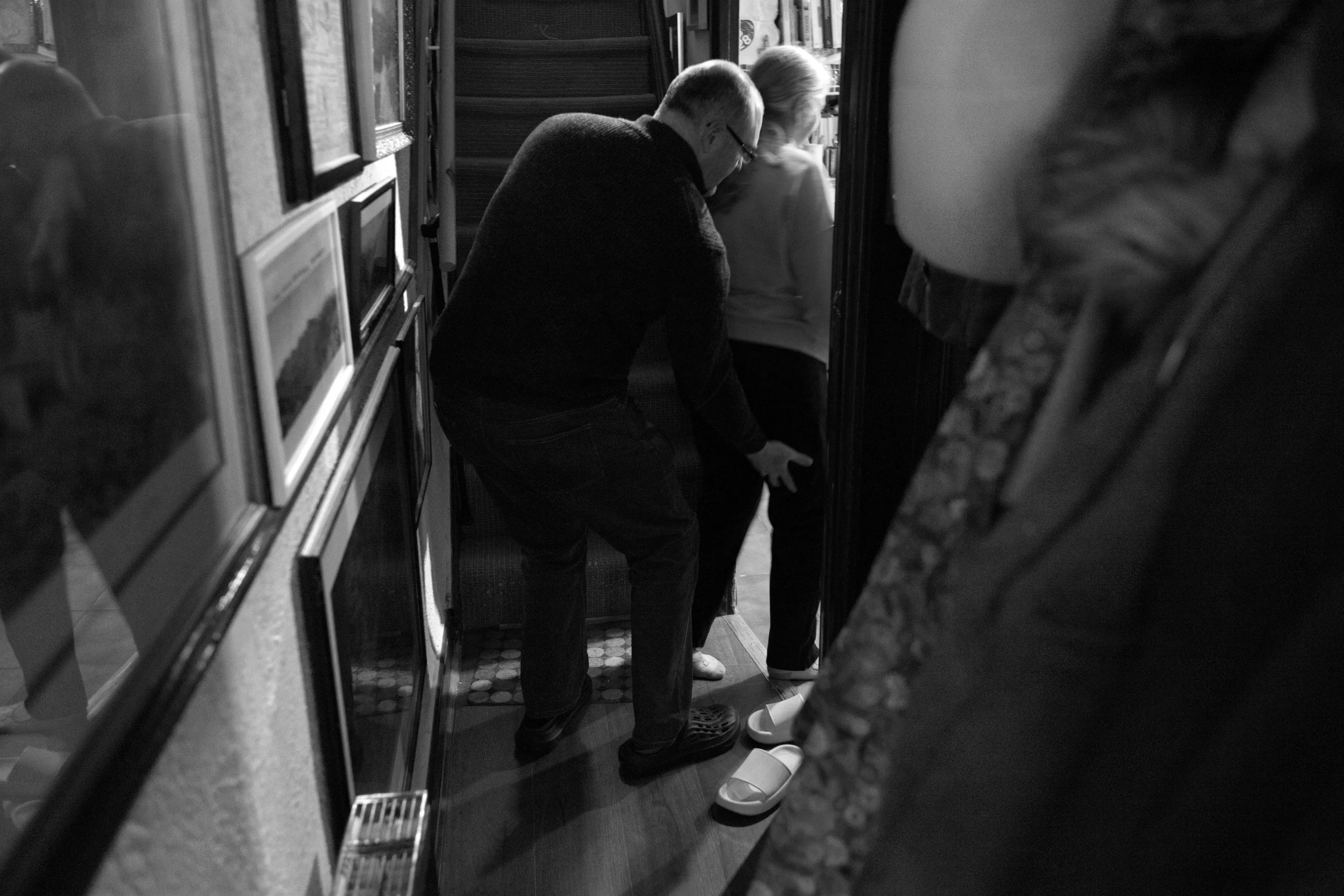 A man bending down at a woman's feet in the hallway doorway, pushing the back of her leg to help restart her movement