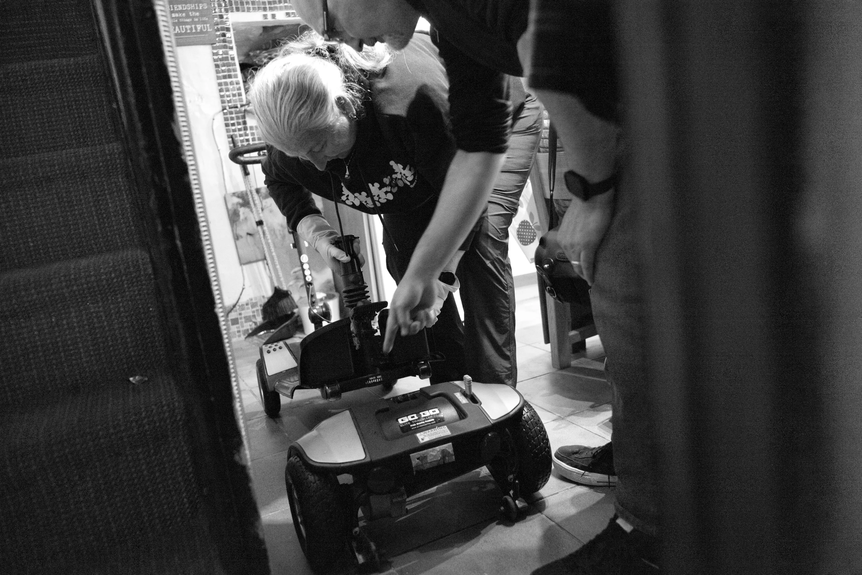 A man and woman crouched over a disassembled mobility scooter on the kitchen floor, examining how to put it together