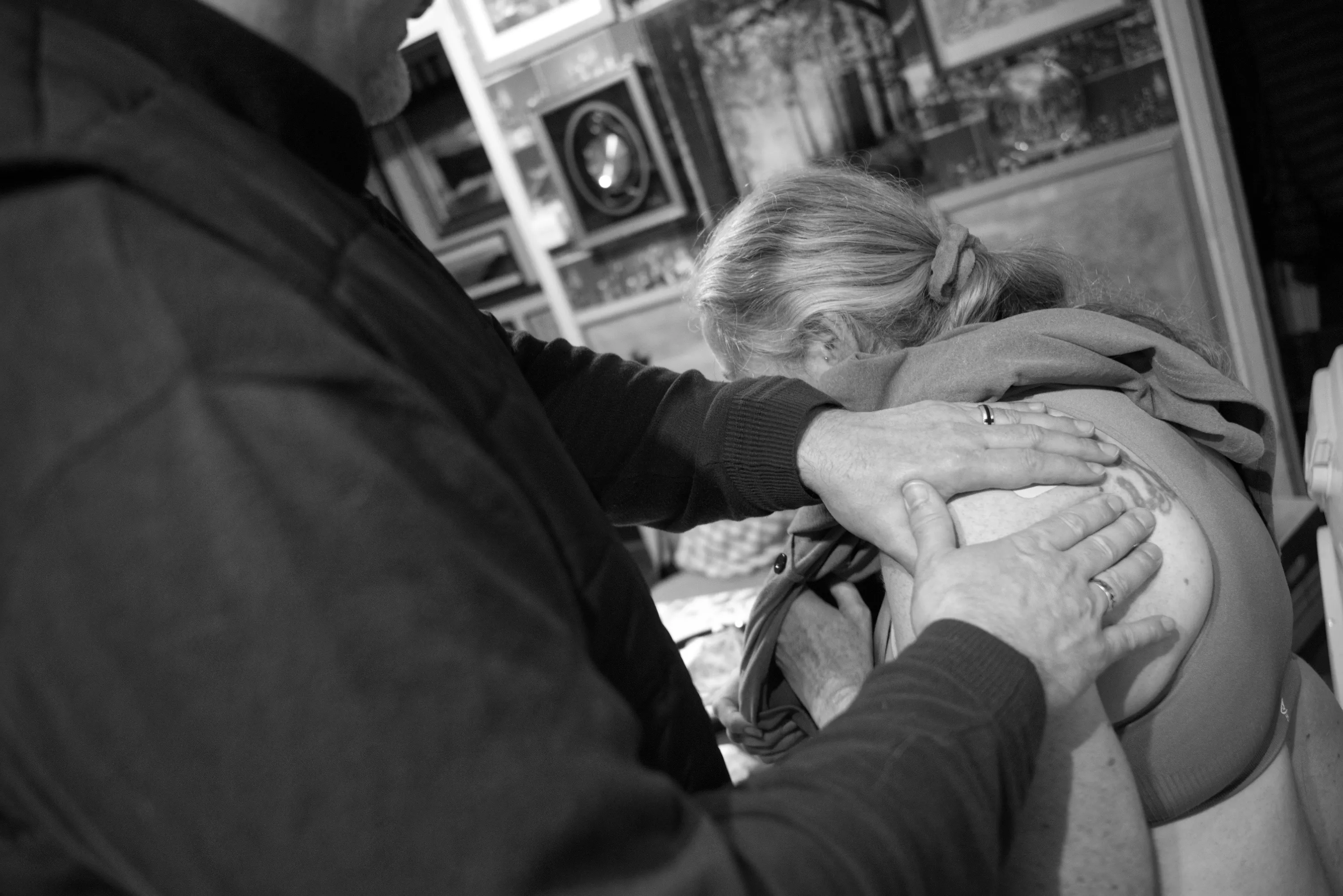 A man pressing both palms firmly onto a transdermal patch on a woman's bare shoulder, her head bowed forward