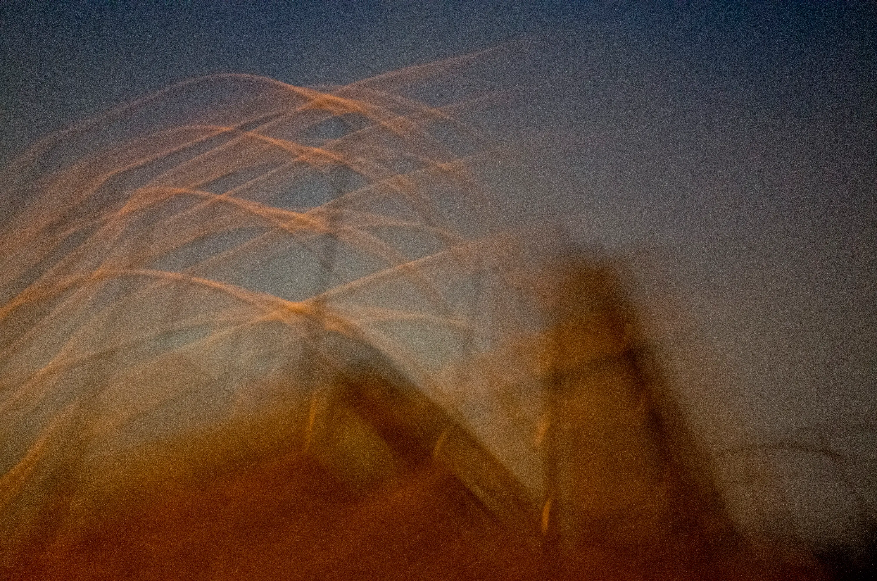 Blurred power lines and structure against a dusk sky with light trails