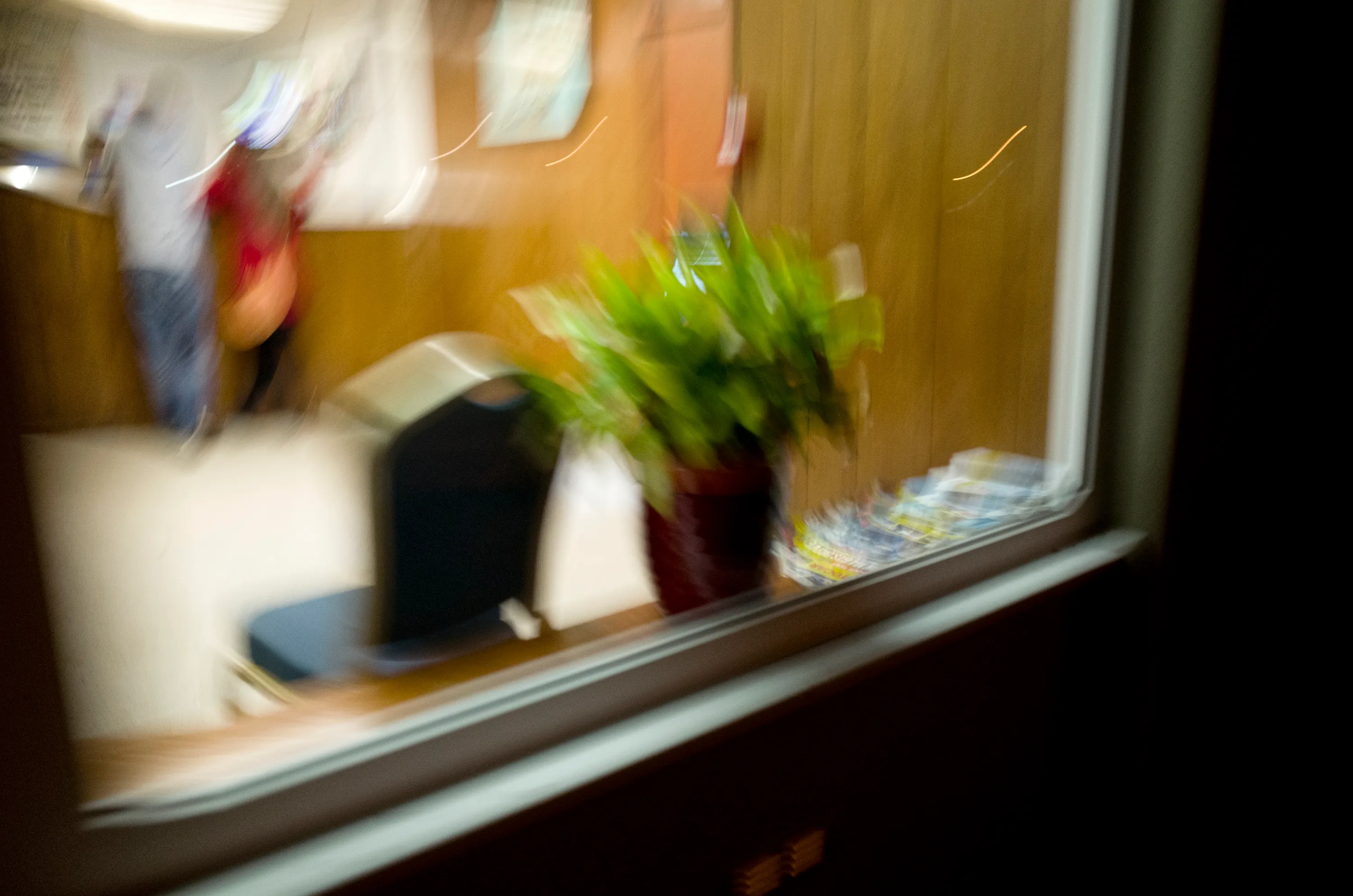 View through a window into a fast-food restaurant with a potted plant and stacked magazines