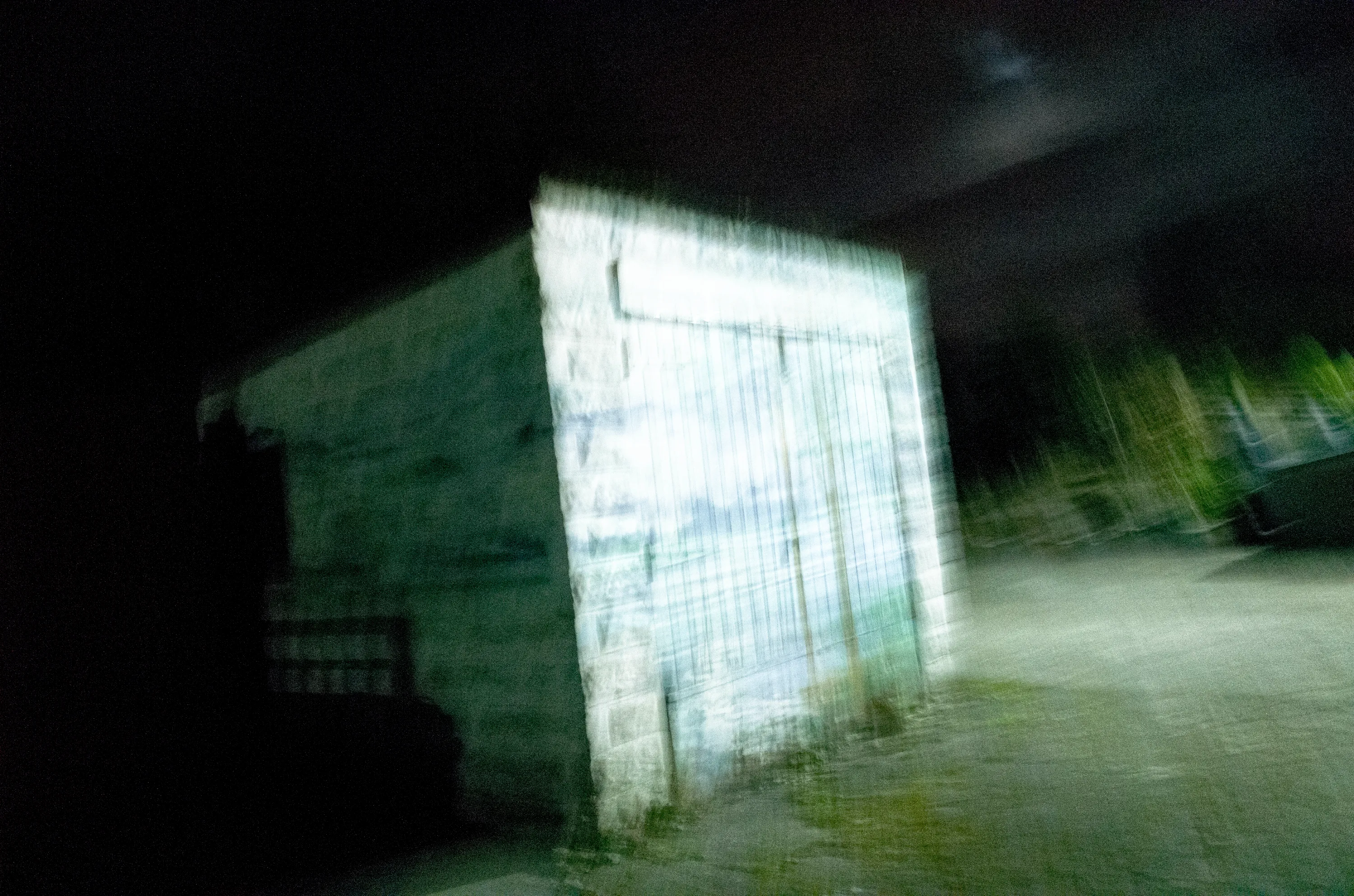 Blurred white outbuilding with graffiti in a dark yard at night