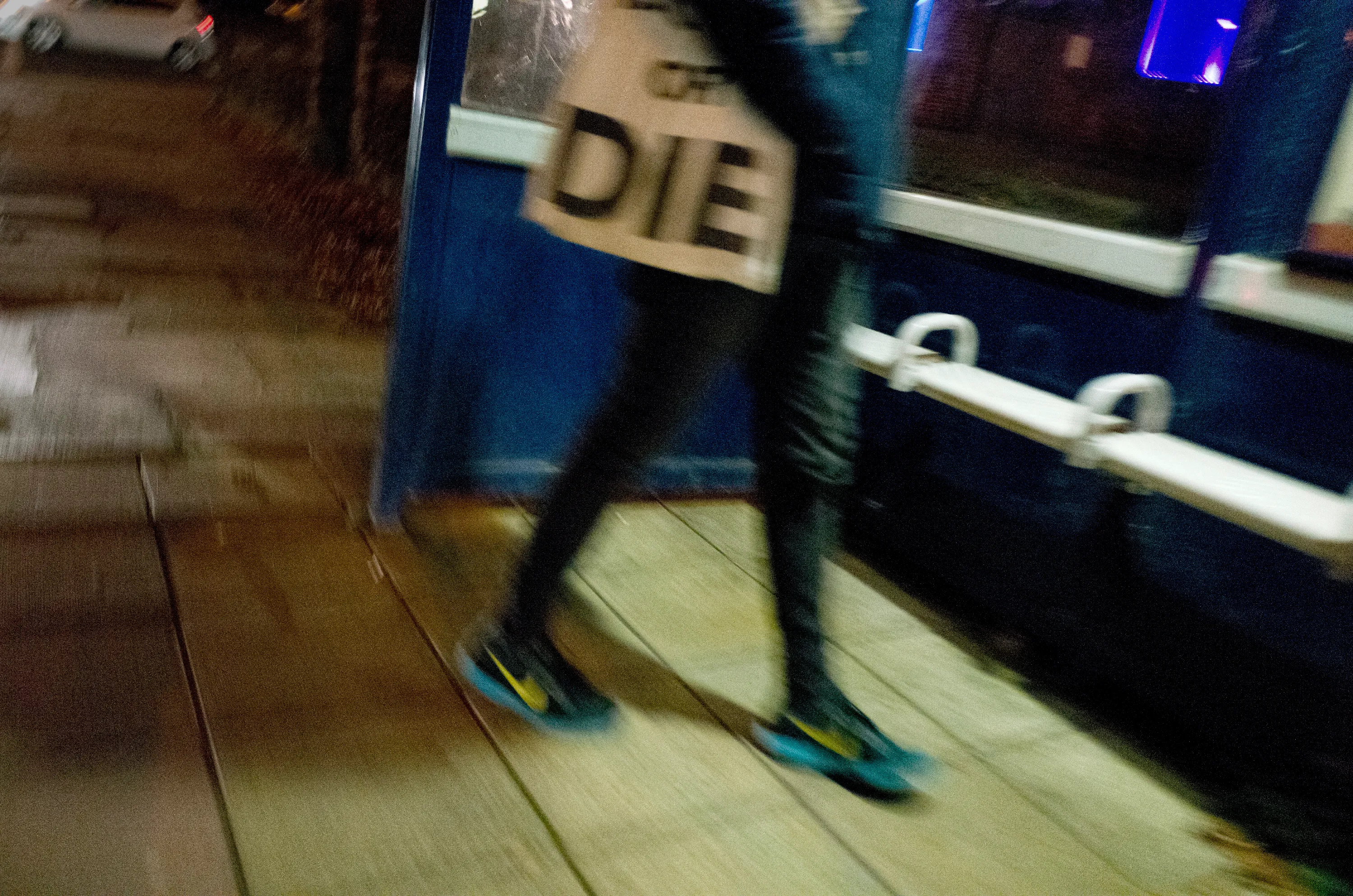 Blurred legs of a person walking past a shop front carrying a bag reading DIE