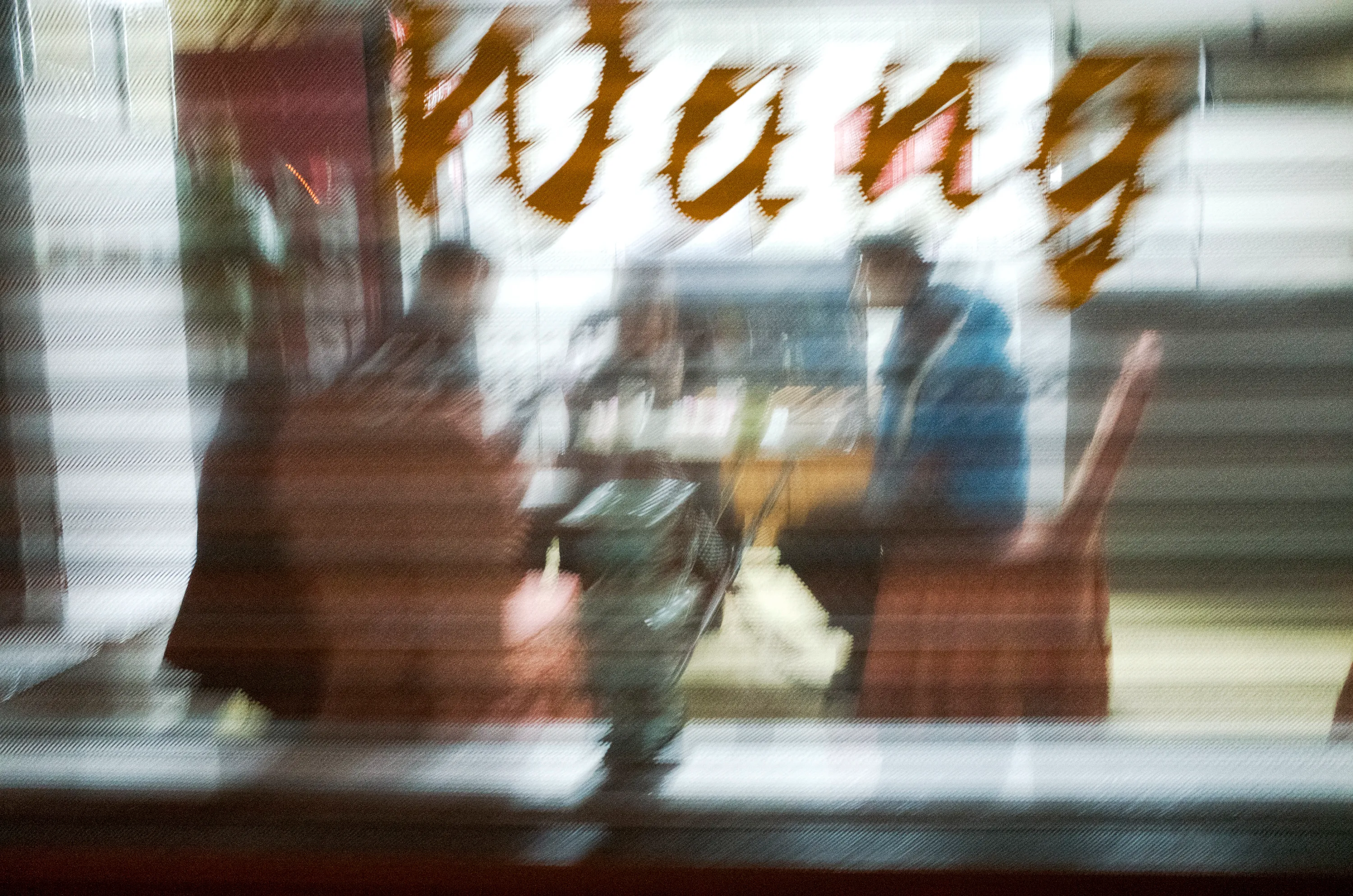 Two people seen through a restaurant window with the word Wang in gold lettering