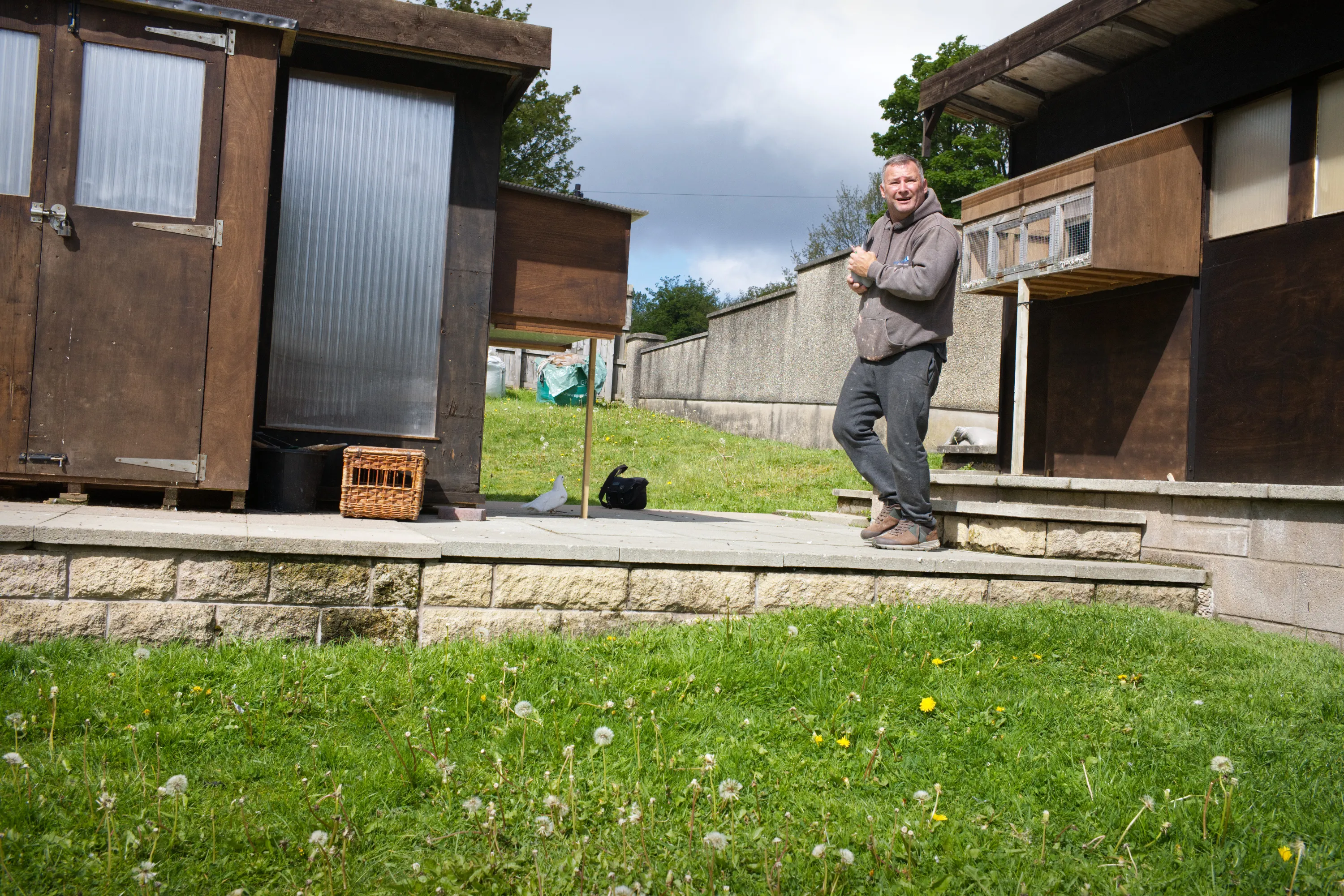 Man standing between wooden lofts in a garden with a wicker basket nearby