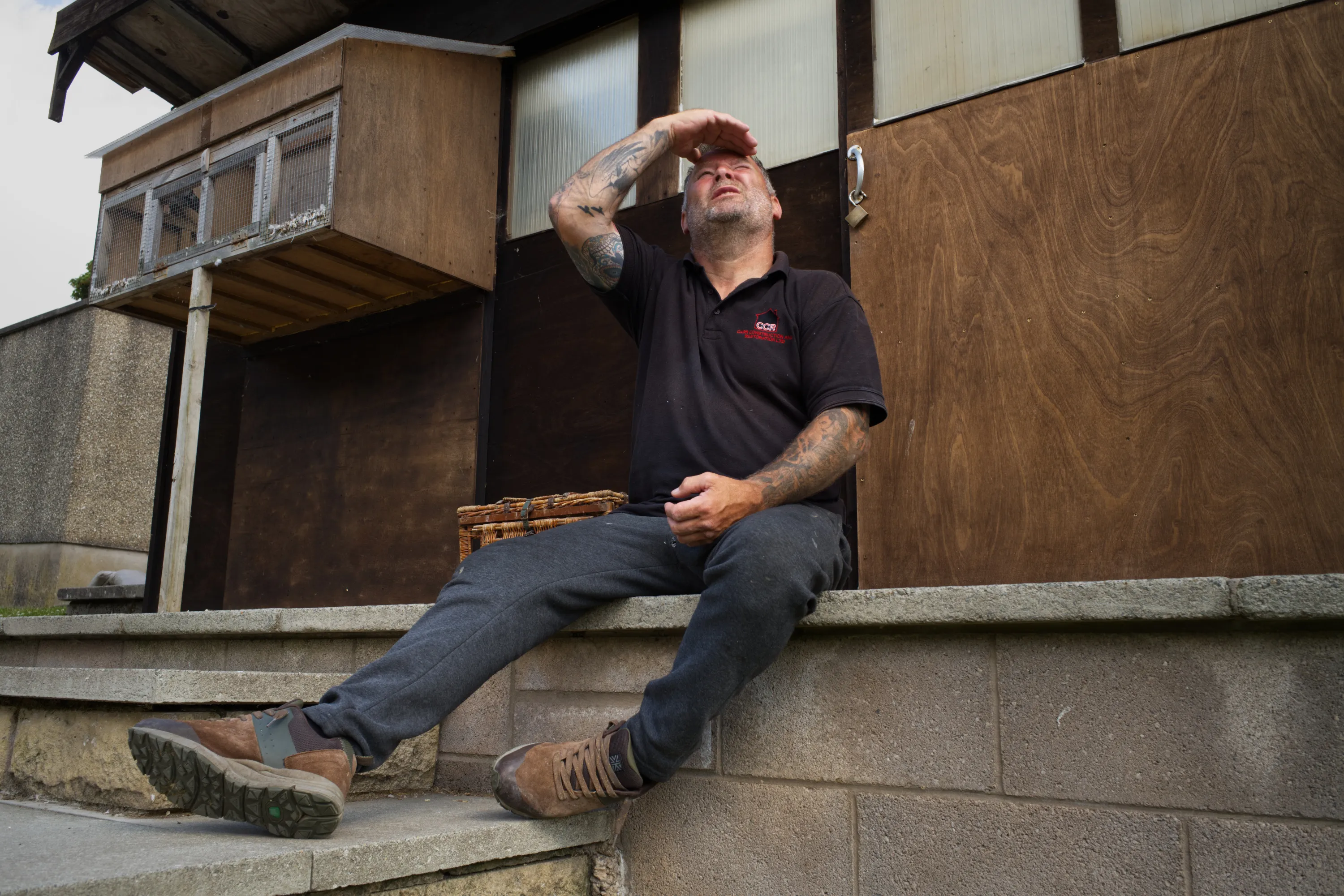Man seated on a ledge outside the loft, shielding his eyes to scan the sky