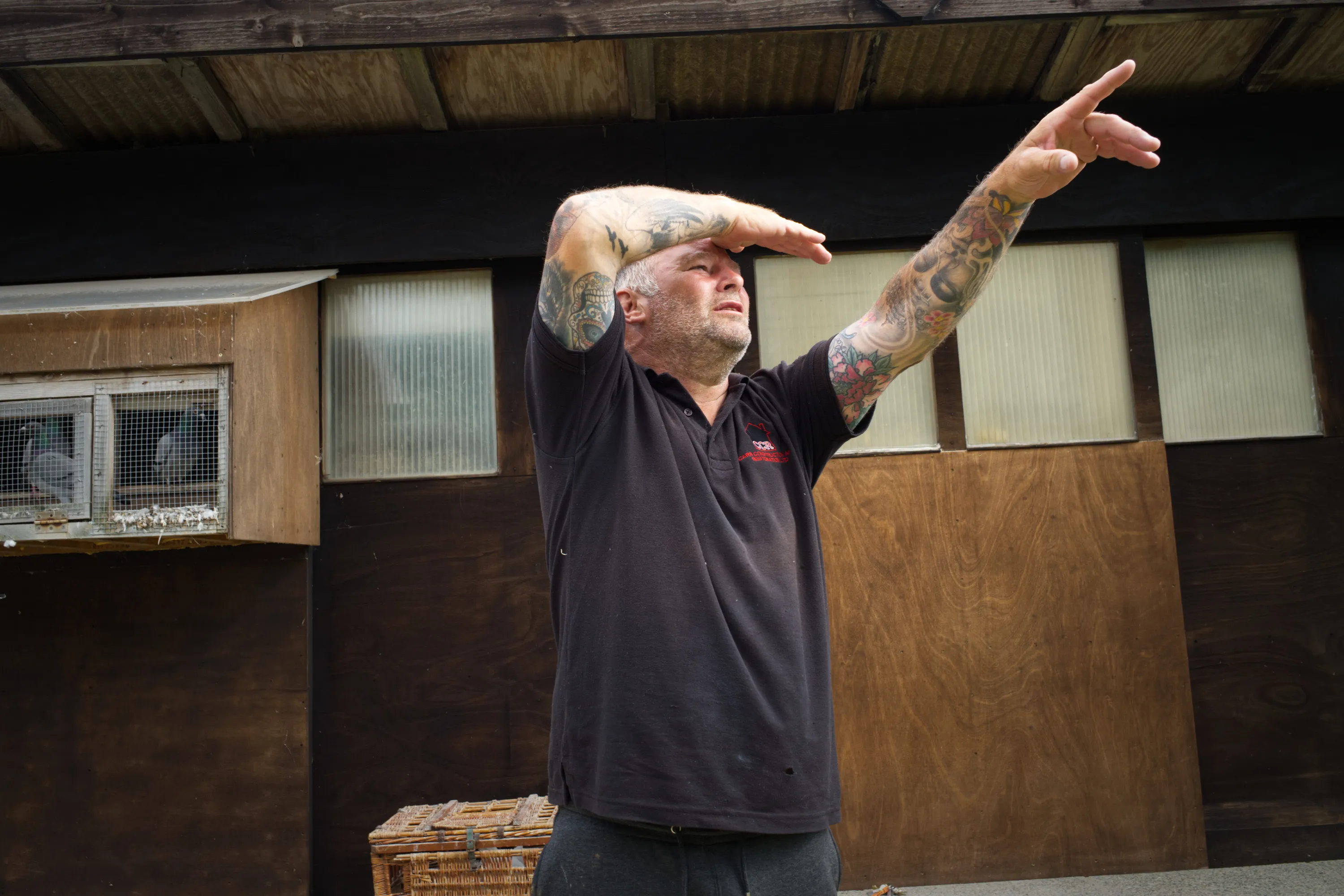 Man standing outside a loft, arm raised and shading his eyes, pointing skyward
