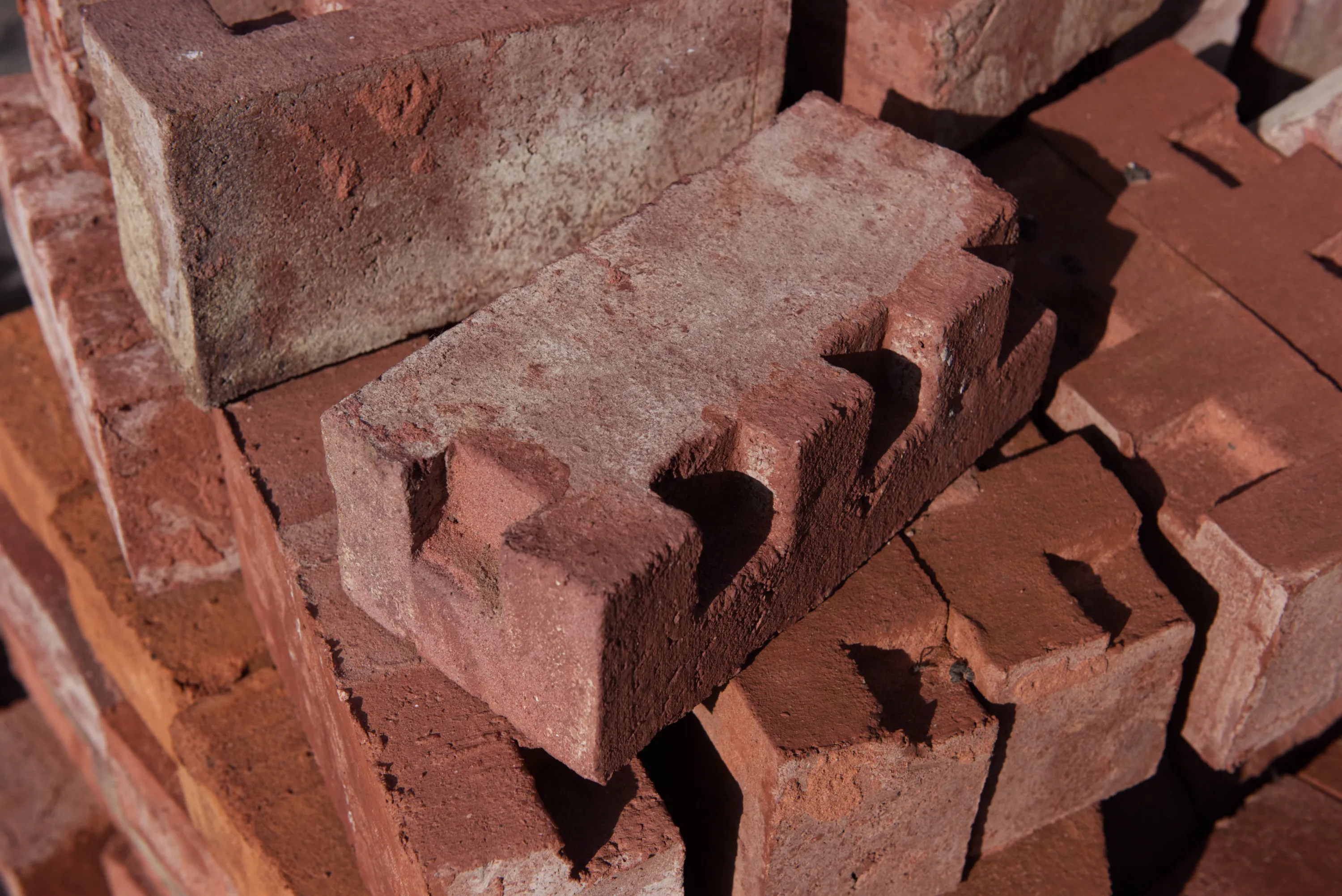 Close-up of rough red bricks with frog indentations, stacked in sunlight