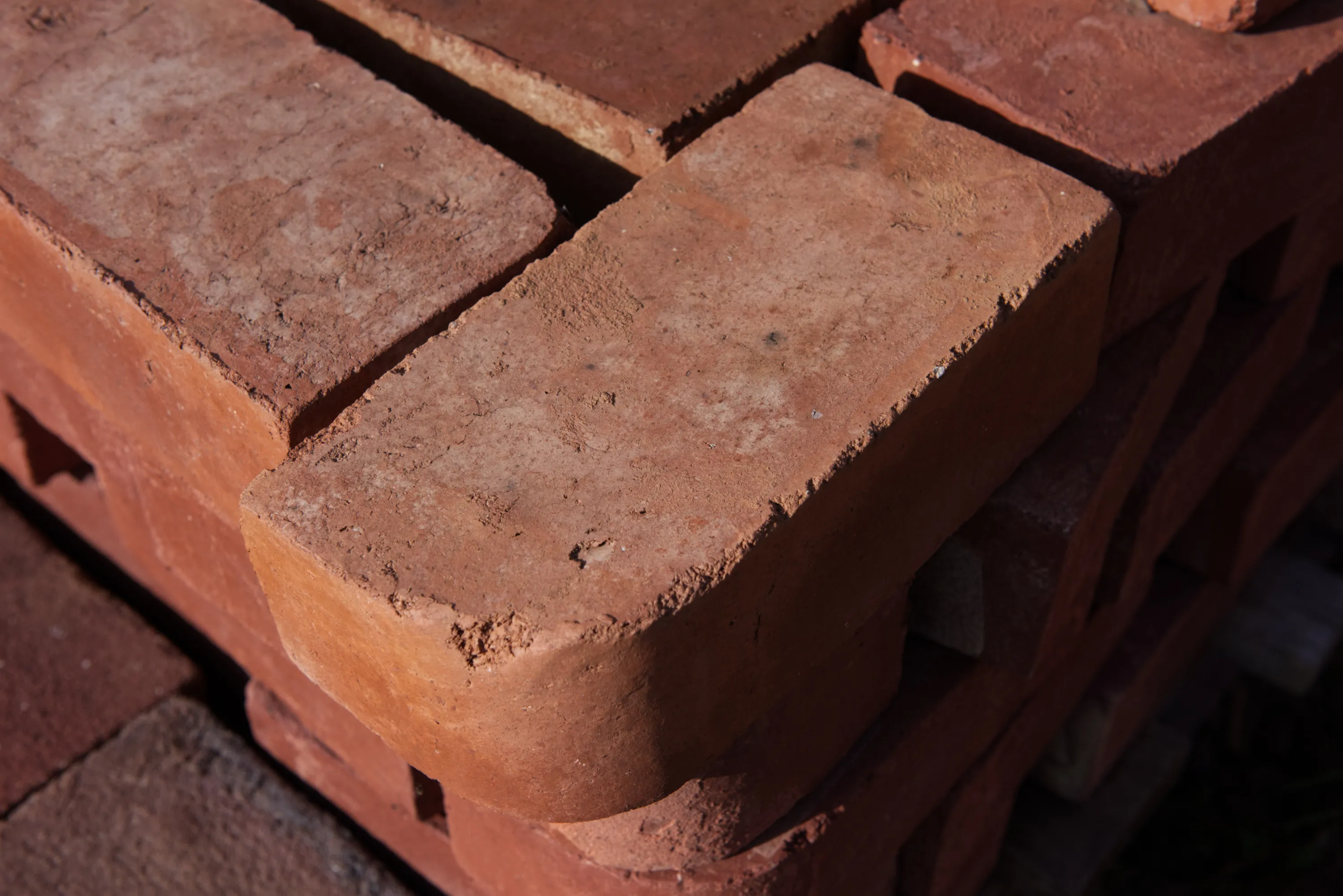 Corner of a pallet of red bricks in sharp sunlight, texture and edges prominent