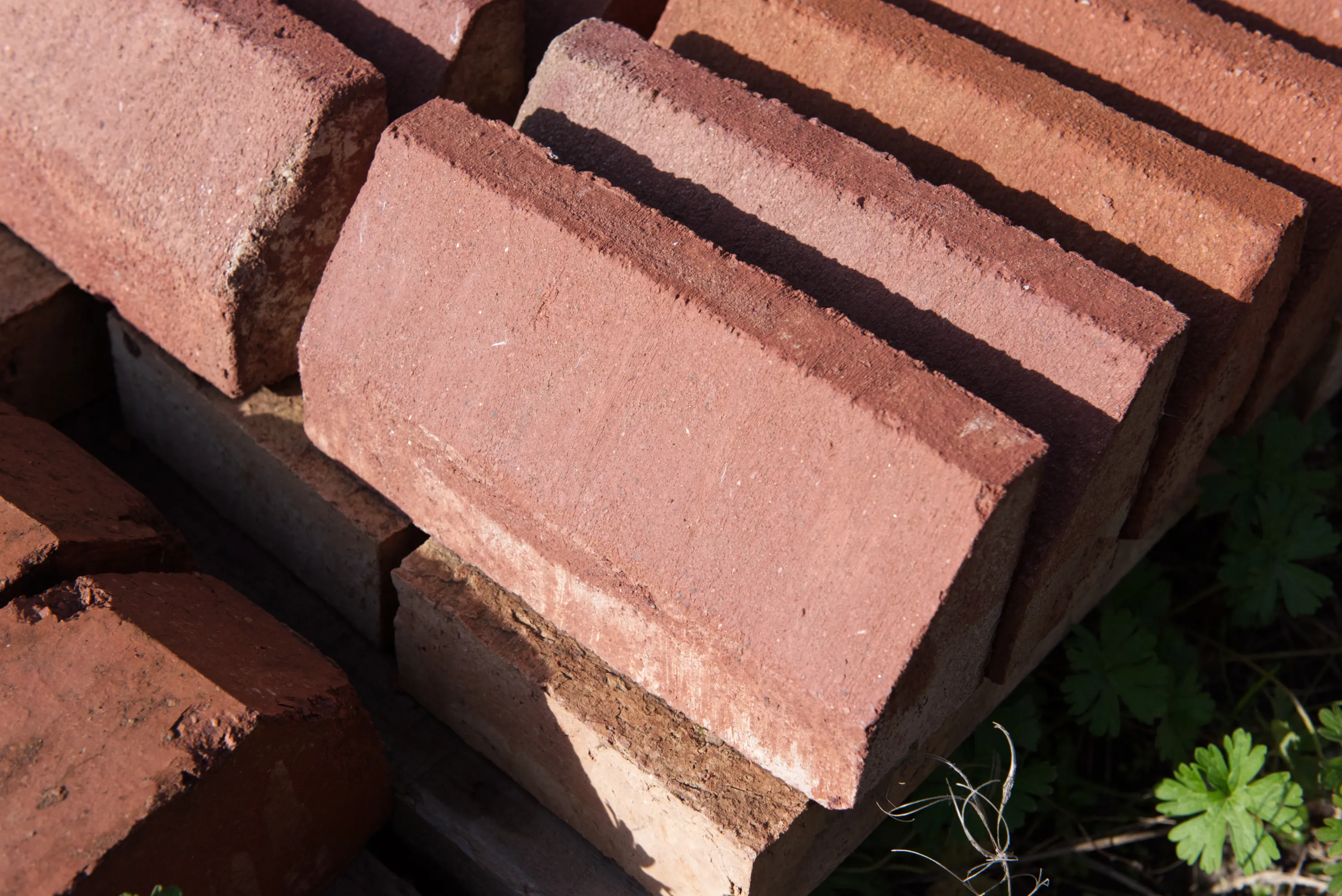 Side view of smooth red coping bricks stacked on a pallet, with vegetation behind