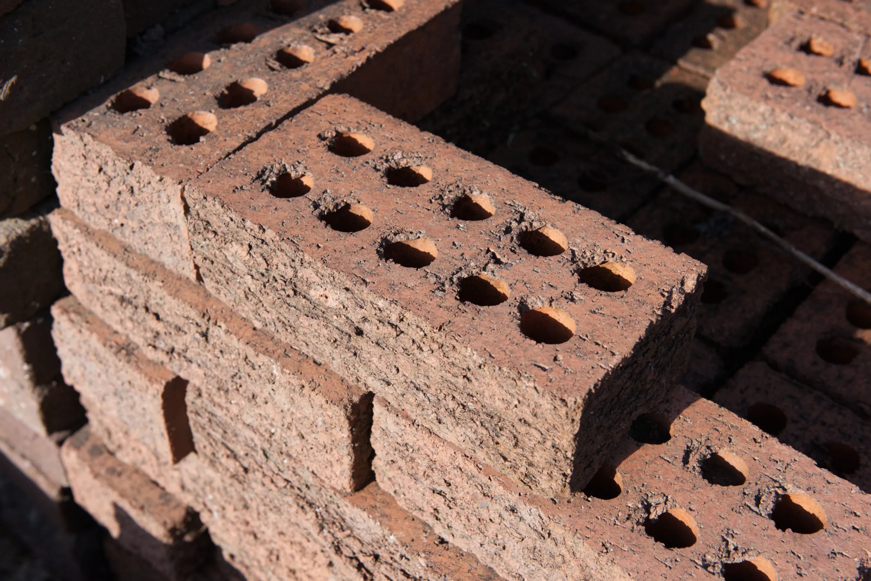 Stack of perforated red bricks showing rows of circular holes along their faces