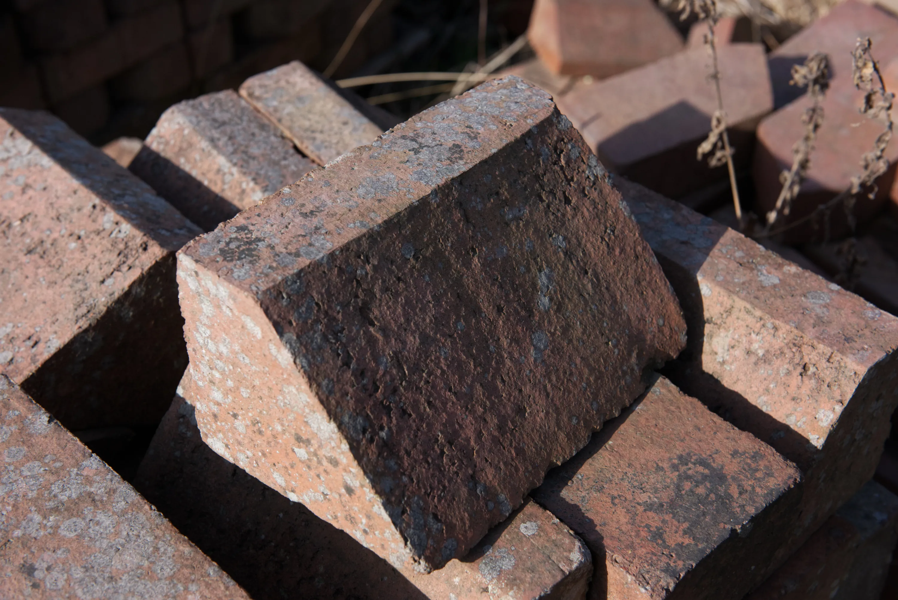 A fire-blackened red brick resting on a pile of worn bricks in sunlight