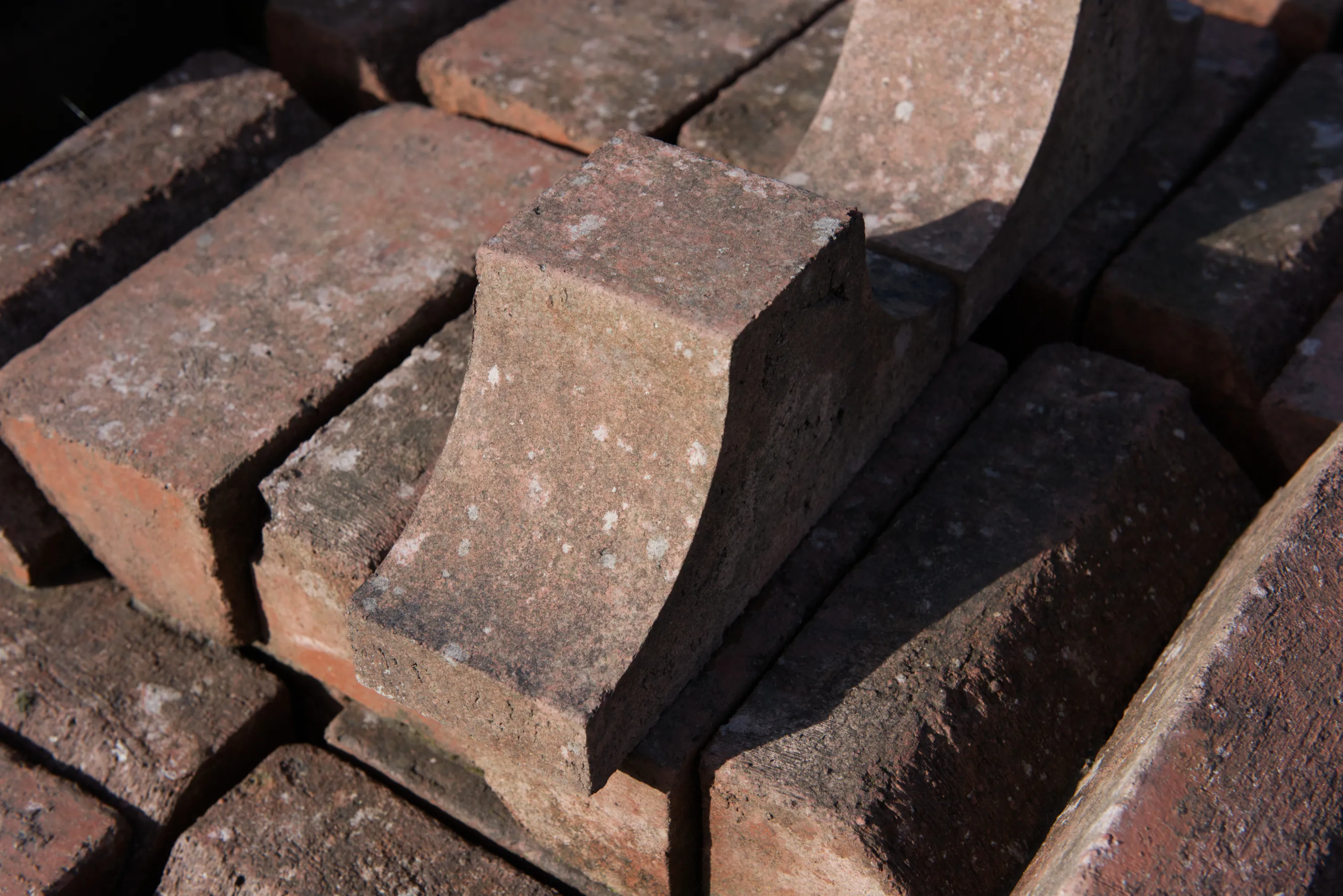A shaped corbel brick with a curved undercut profile, resting on a stack of weathered bricks