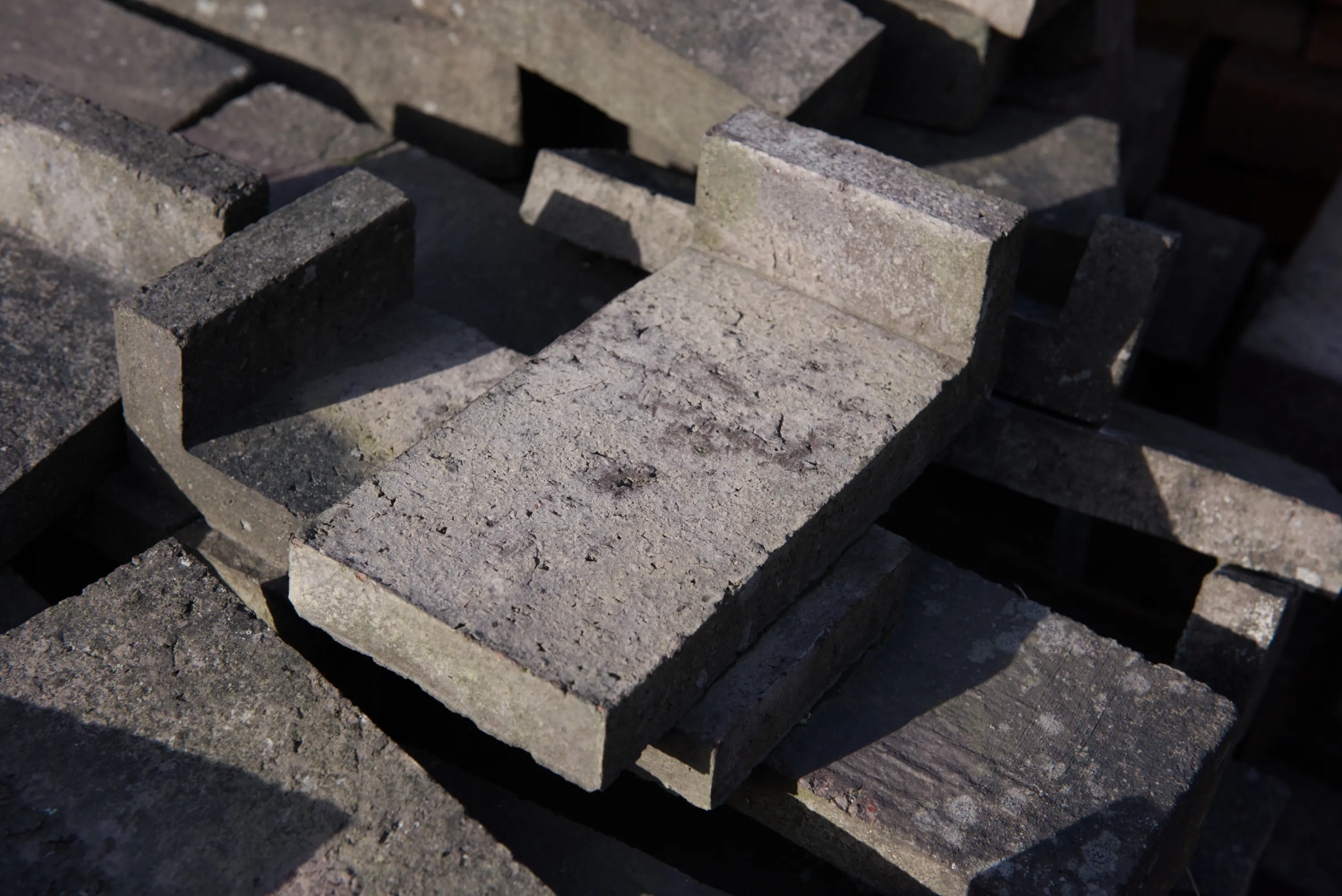 Grey bricks with a rebated profile scattered in sunlight, casting strong shadows