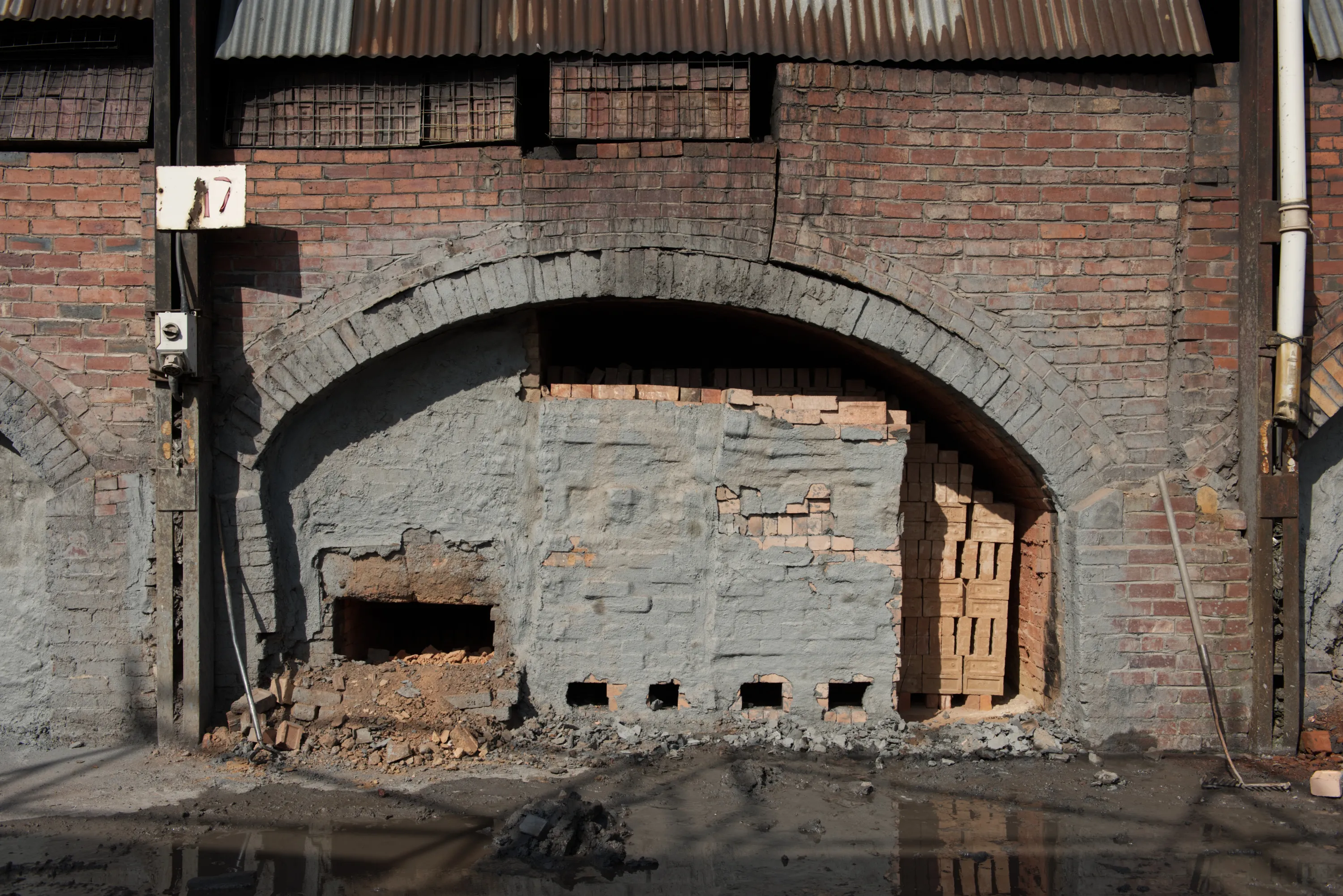A kiln arch numbered 17, its opening nearly sealed with a rough brick wall, rubble on the ground