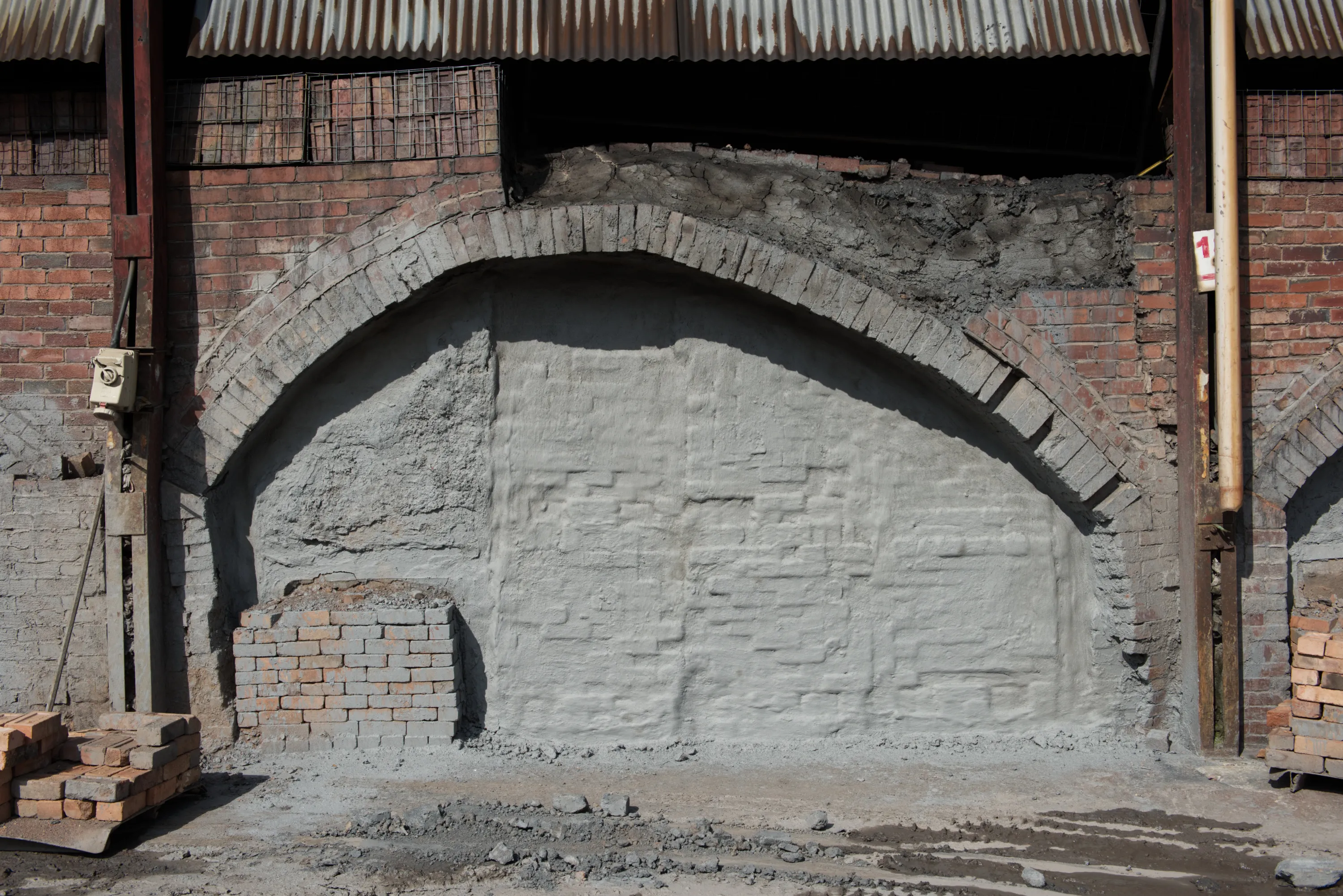 A kiln arch sealed with a smooth grey clay render, small vents at the base, bricks stacked to one side