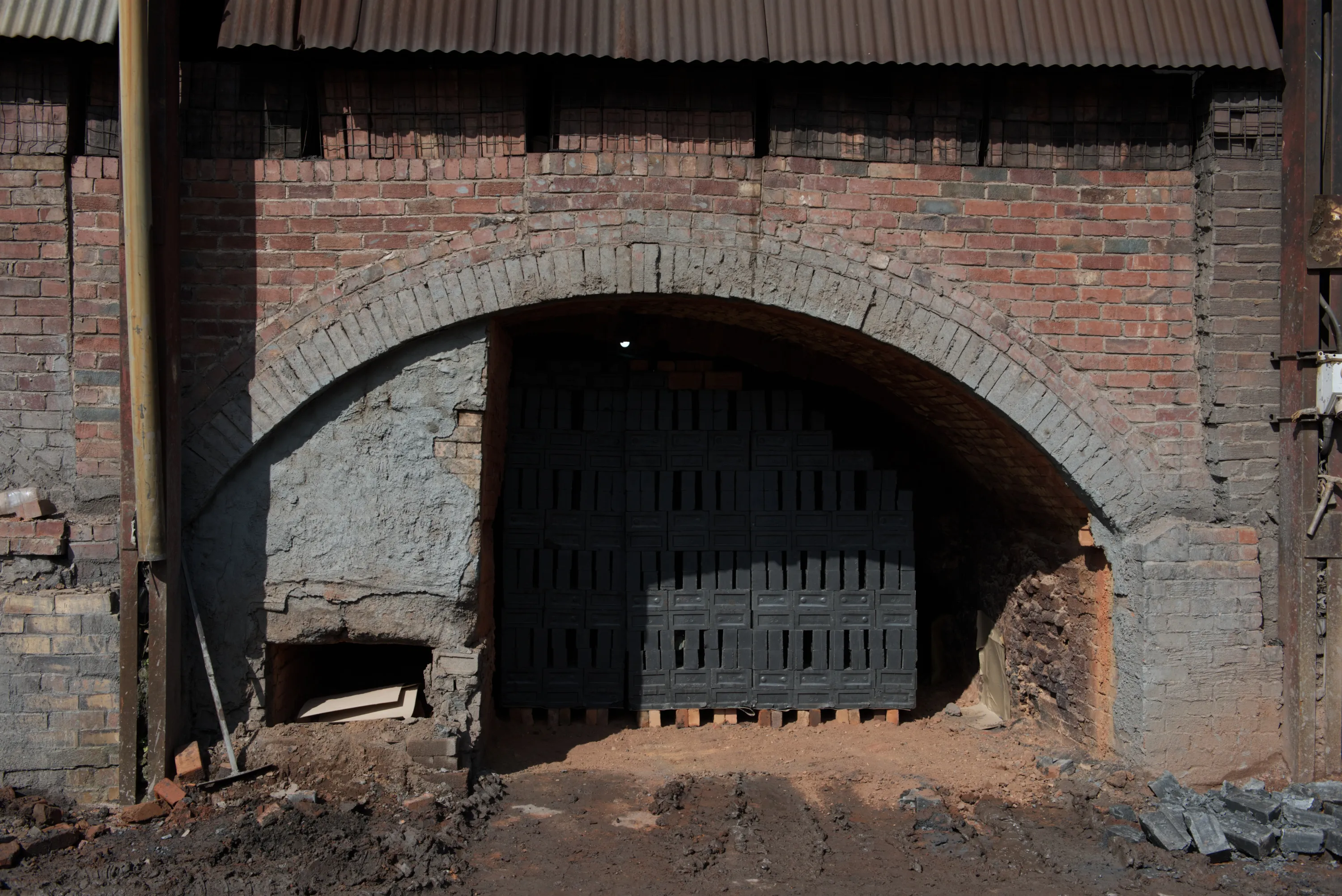A kiln arch in darkness, its interior filled with black brick setters on pallets