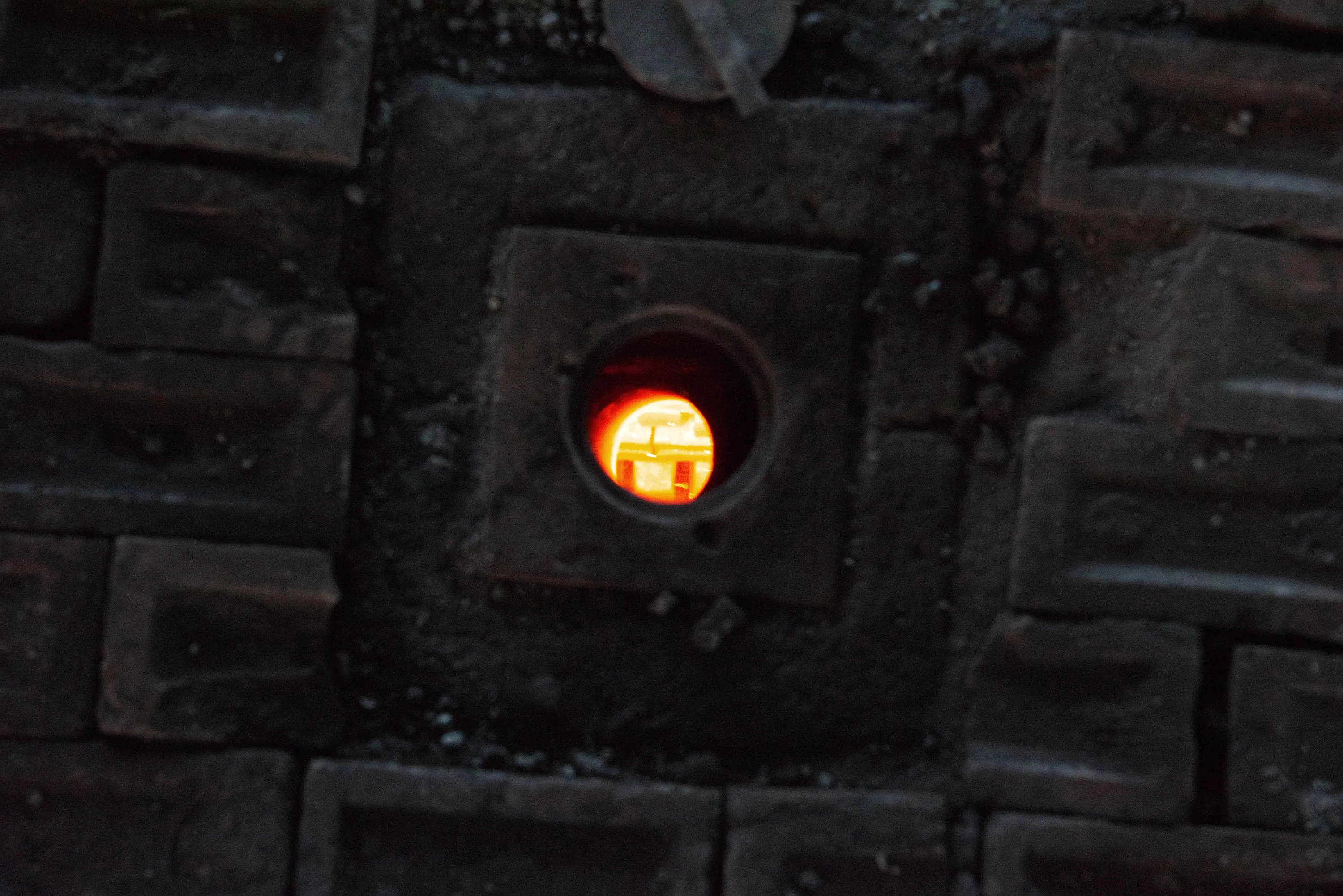 A glowing orange peephole in a dark kiln crown, surrounded by the tops of dark brick setters