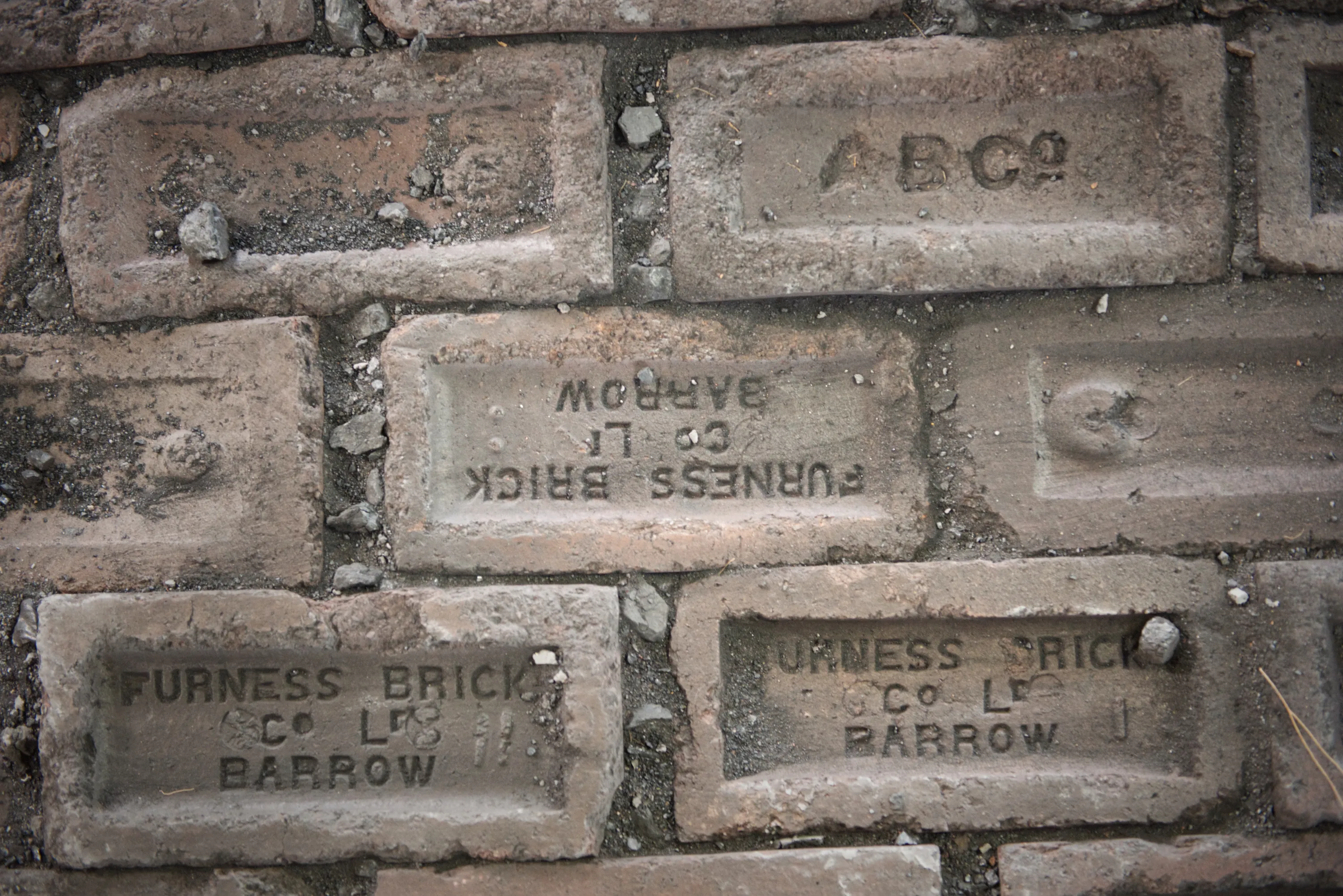 Old bricks laid face-down in a wall, stamped Furness Brick Co Ltd Barrow, some inverted