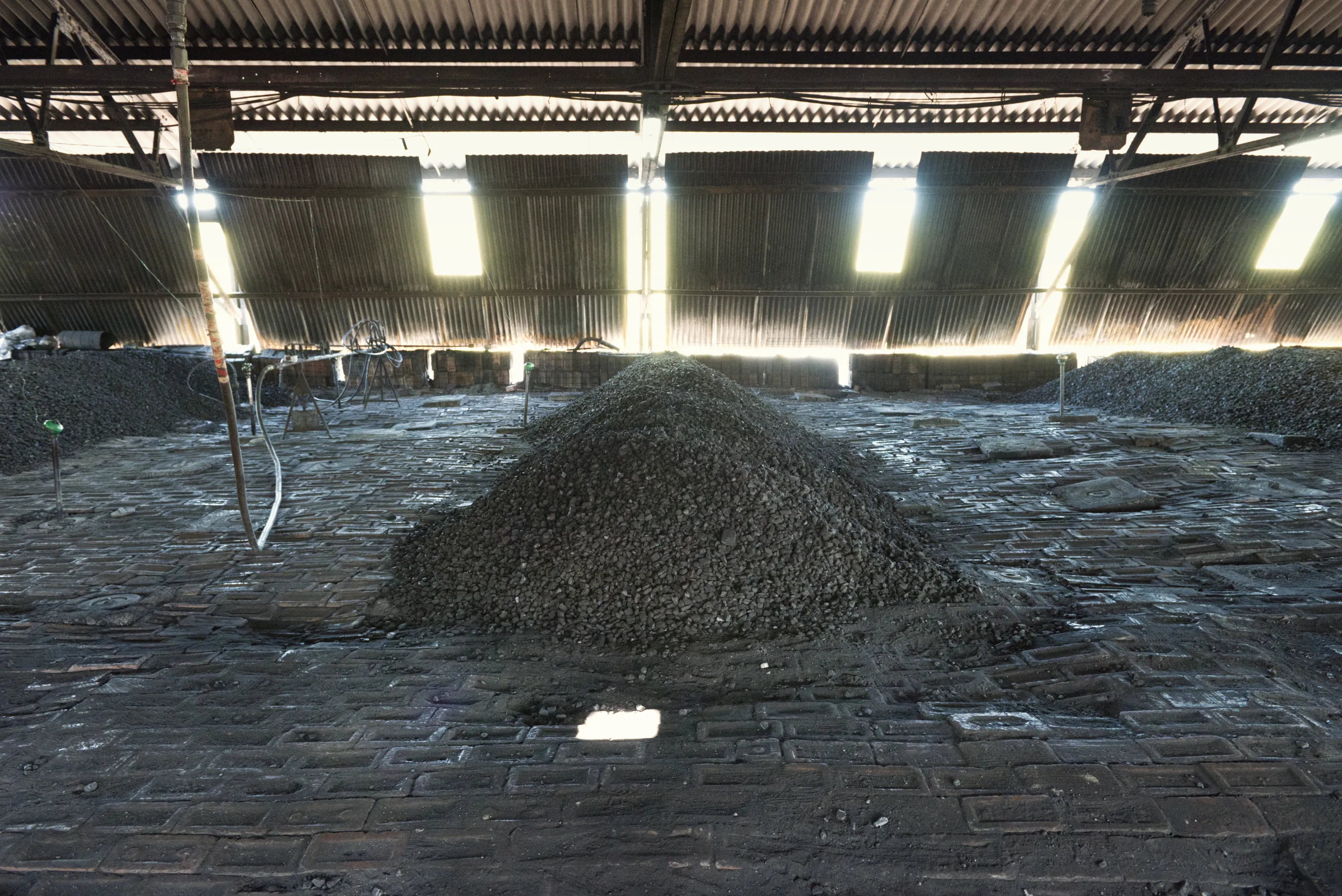 A large mound of coal inside a dark industrial shed, light filtering through the roof
