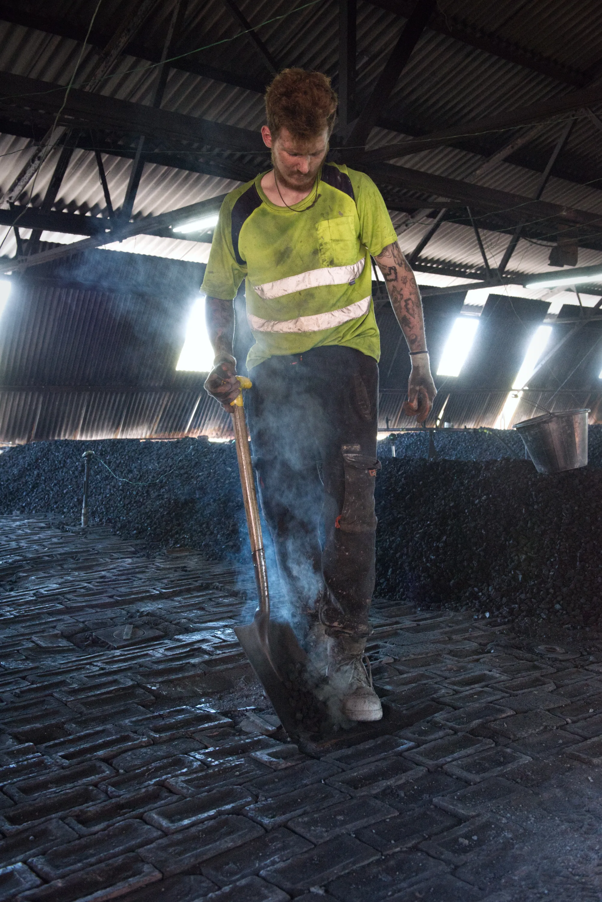 A worker in a hi-vis vest standing amid steam or smoke in a coal store, holding a shovel
