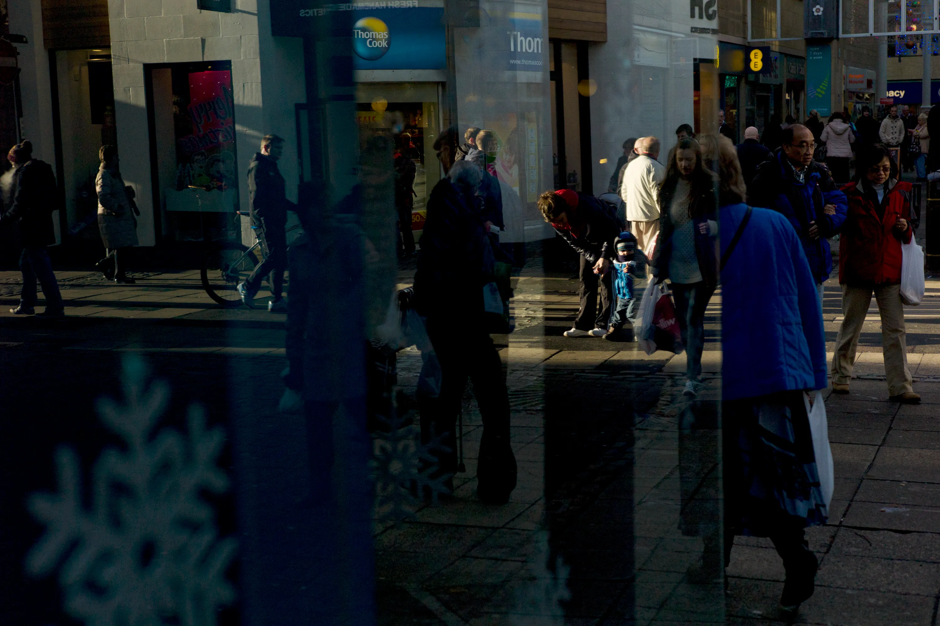 Busy pedestrian street reflected in shop glass, snowflake decal in the foreground