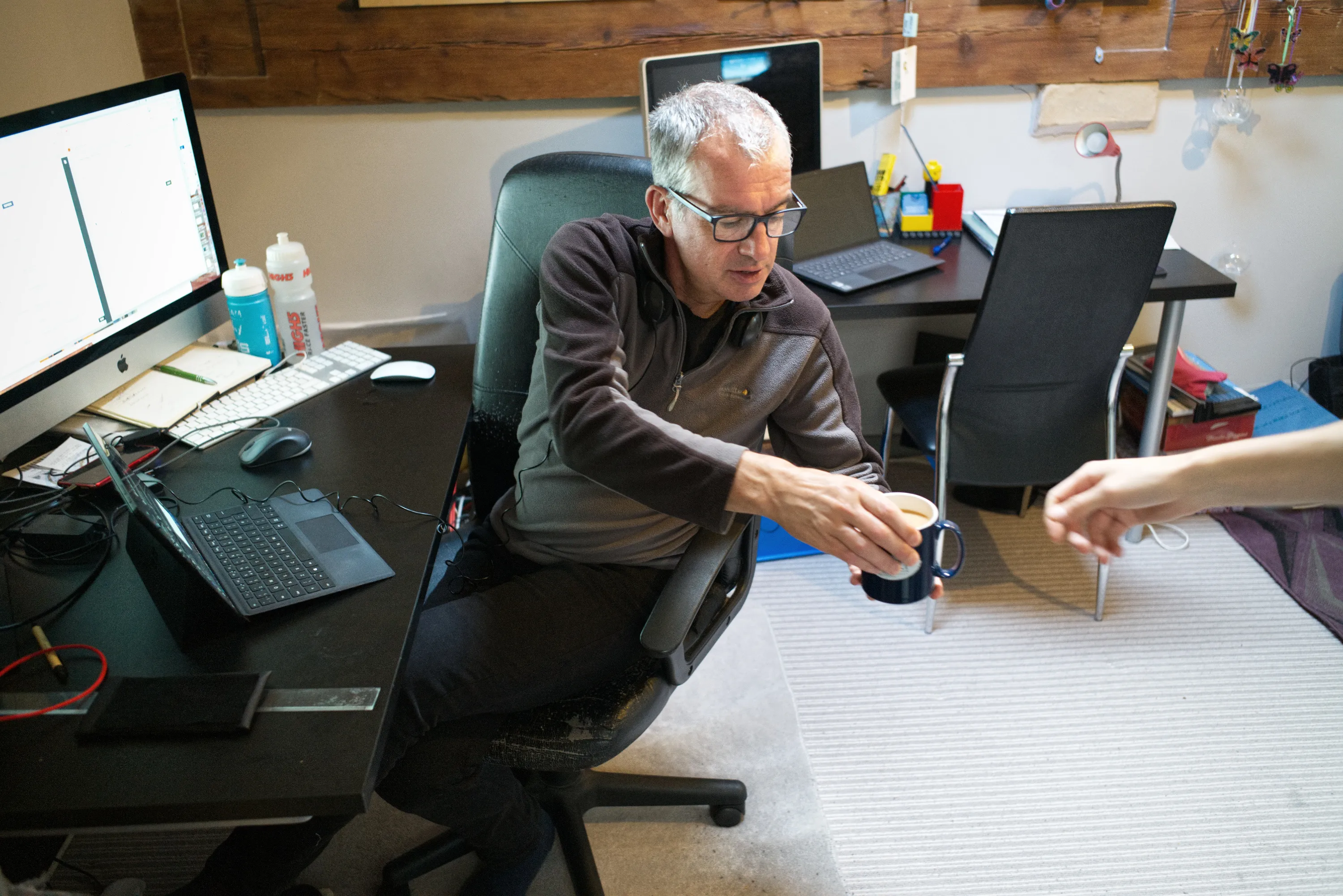 Man in an office chair receiving a mug, surrounded by multiple monitors