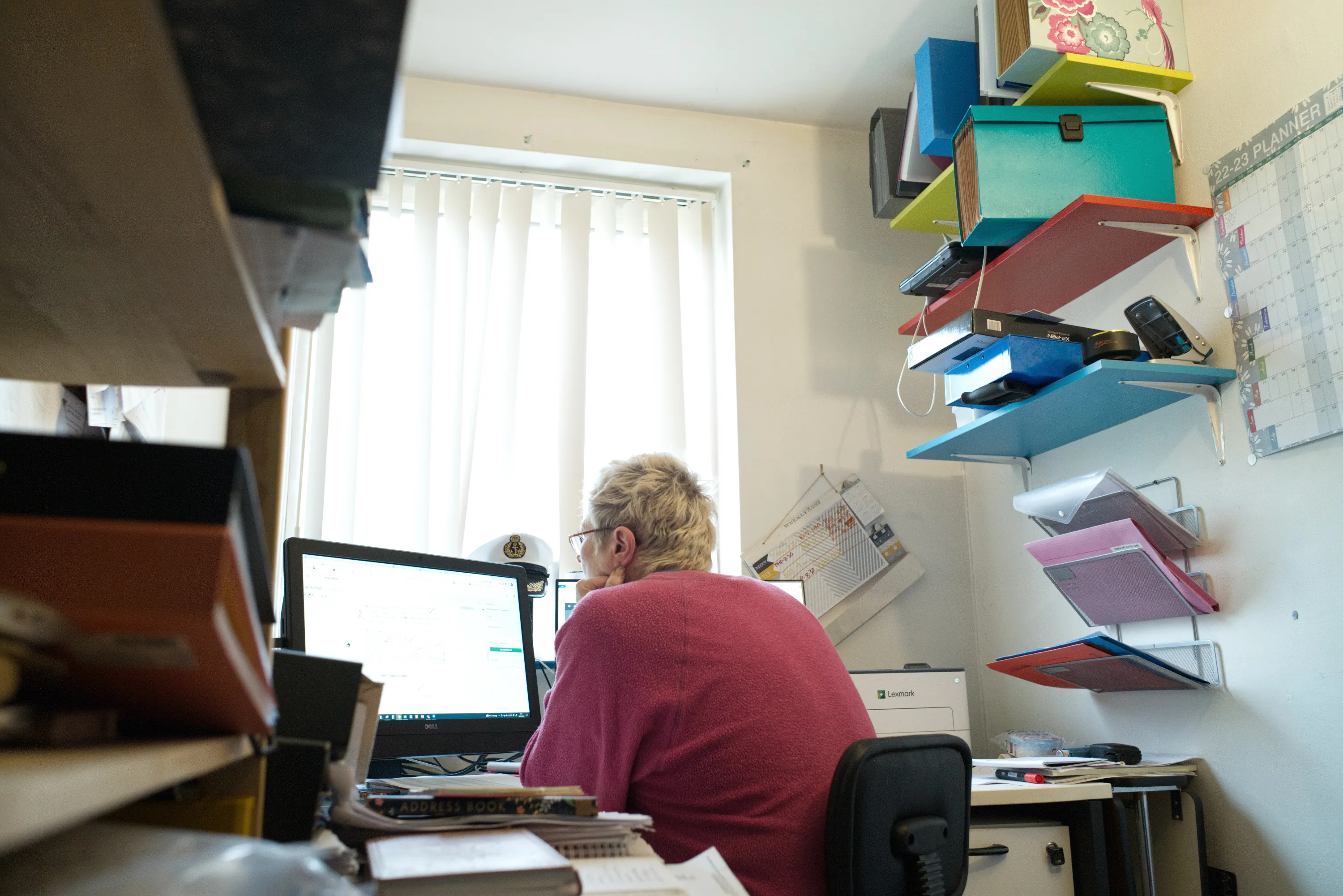 Person at a monitor in a small room lined with colourful stacked storage boxes